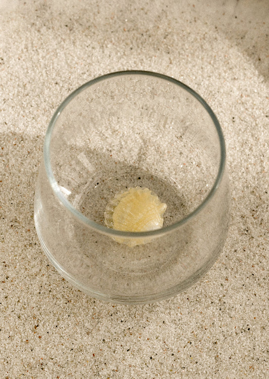 A clear stemless glass with three-dimensional shell detail at bottom of glass.
