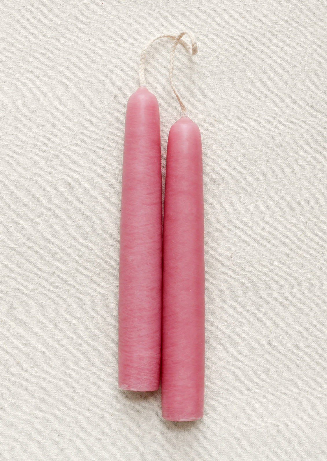Two pink candles on a textured beige surface