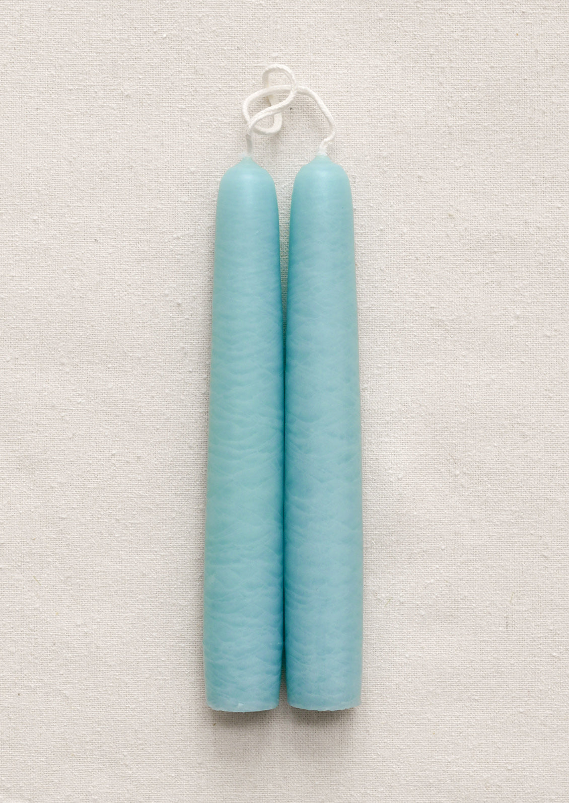 Two light blue ribbed candles hanging on a textured gray background