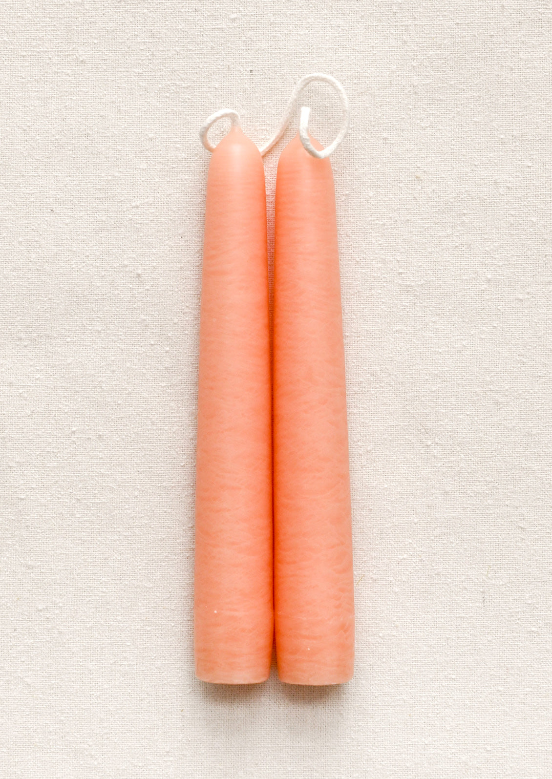 Two peach-colored candles with wicks on a textured beige background