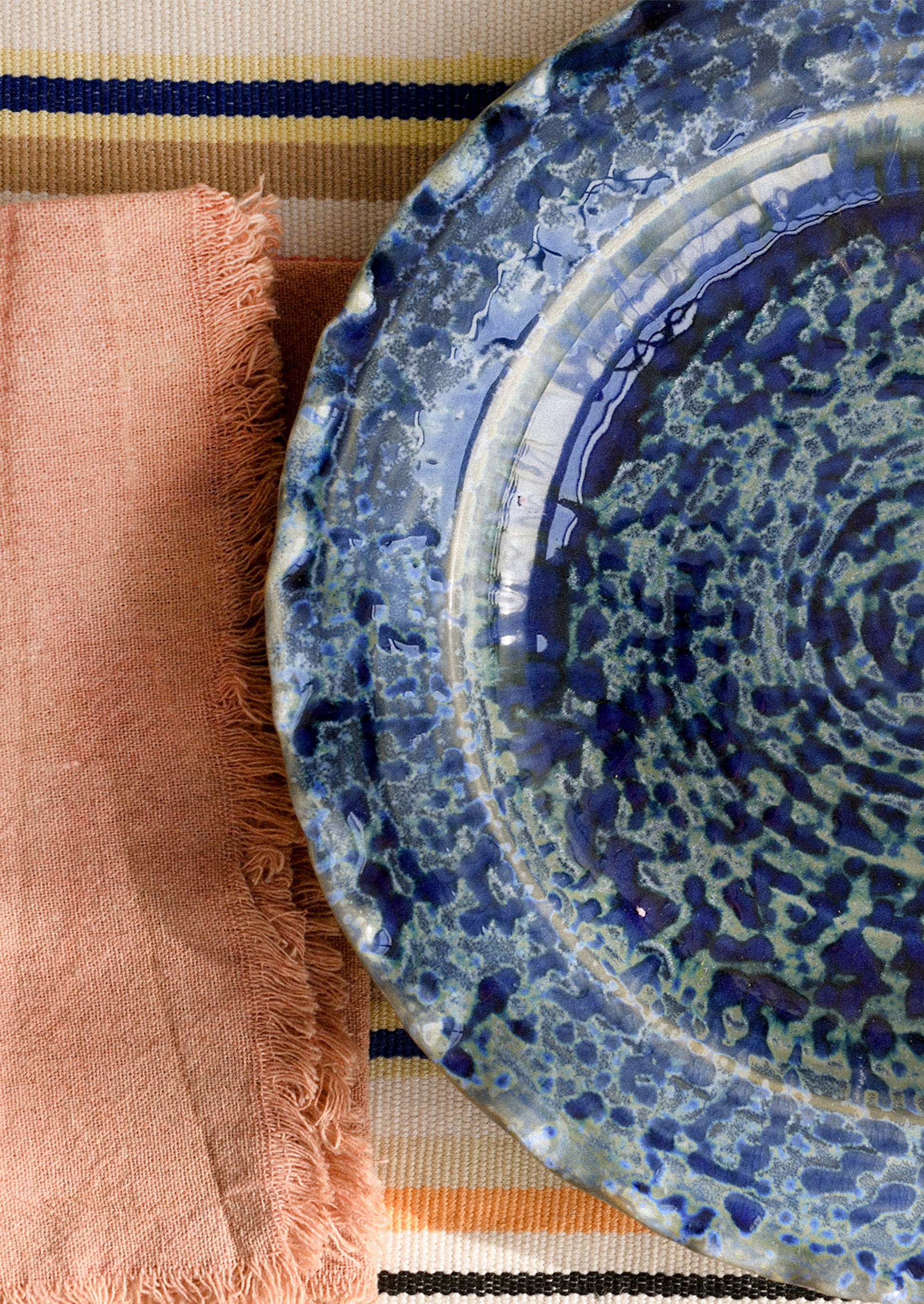 Blue ceramic plate with mottled glaze on a striped fabric background