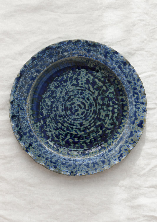Blue ceramic plate with speckled pattern on a white background