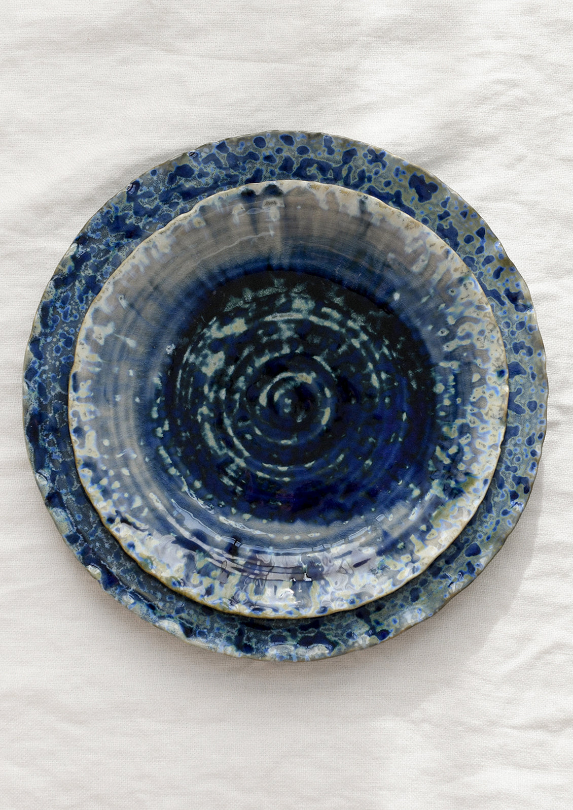 Stack of blue ceramic plates with a mottled glaze on a white surface.