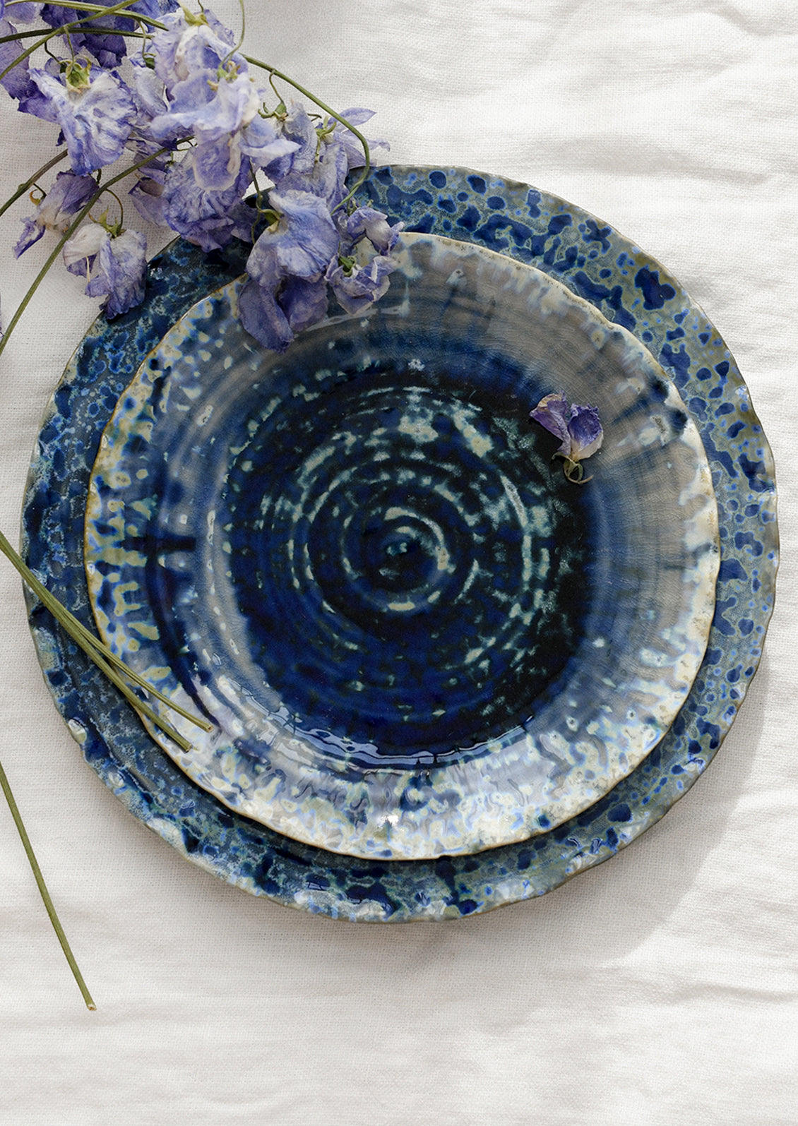 Stack of blue ceramic plates with a mottled glaze on a white surface with purple flowers.