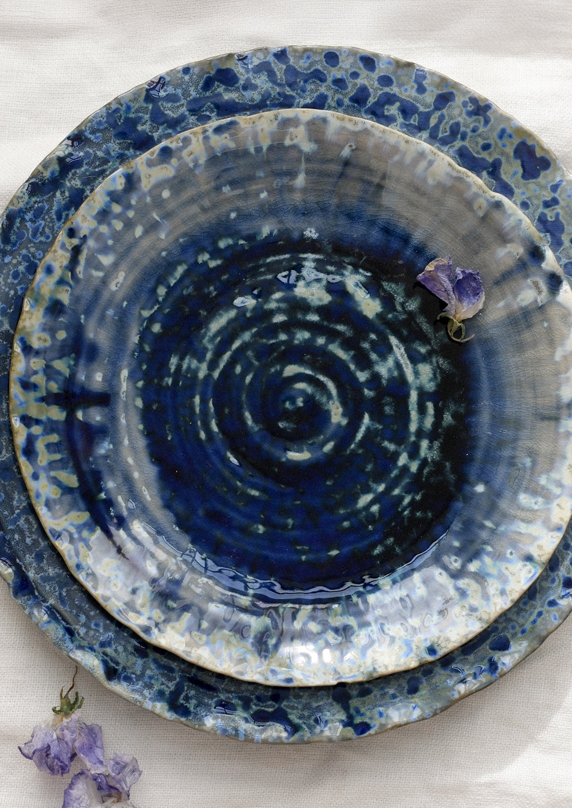 Stack of blue ceramic plates with a mottled glaze on a white surface with purple flowers.