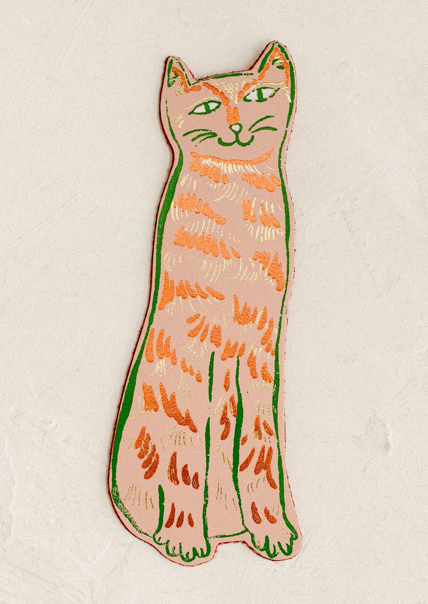 A die-cut leather bookmark in the shape of a cat, in peach color.
