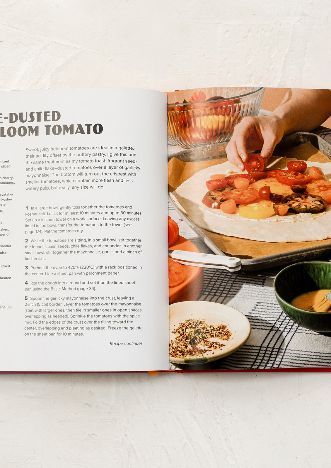 Open cookbook showing a recipe with a person preparing food in the background