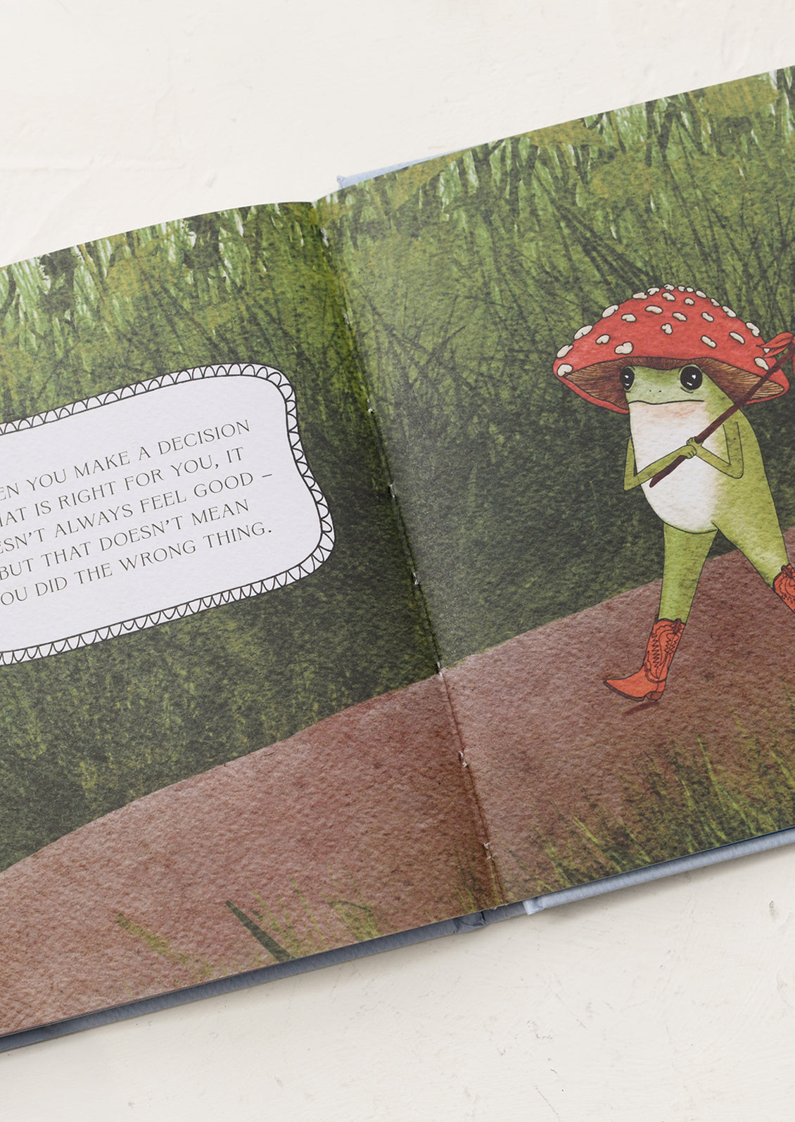 Illustrated book page with a frog character wearing a red mushroom hat on a forest background.