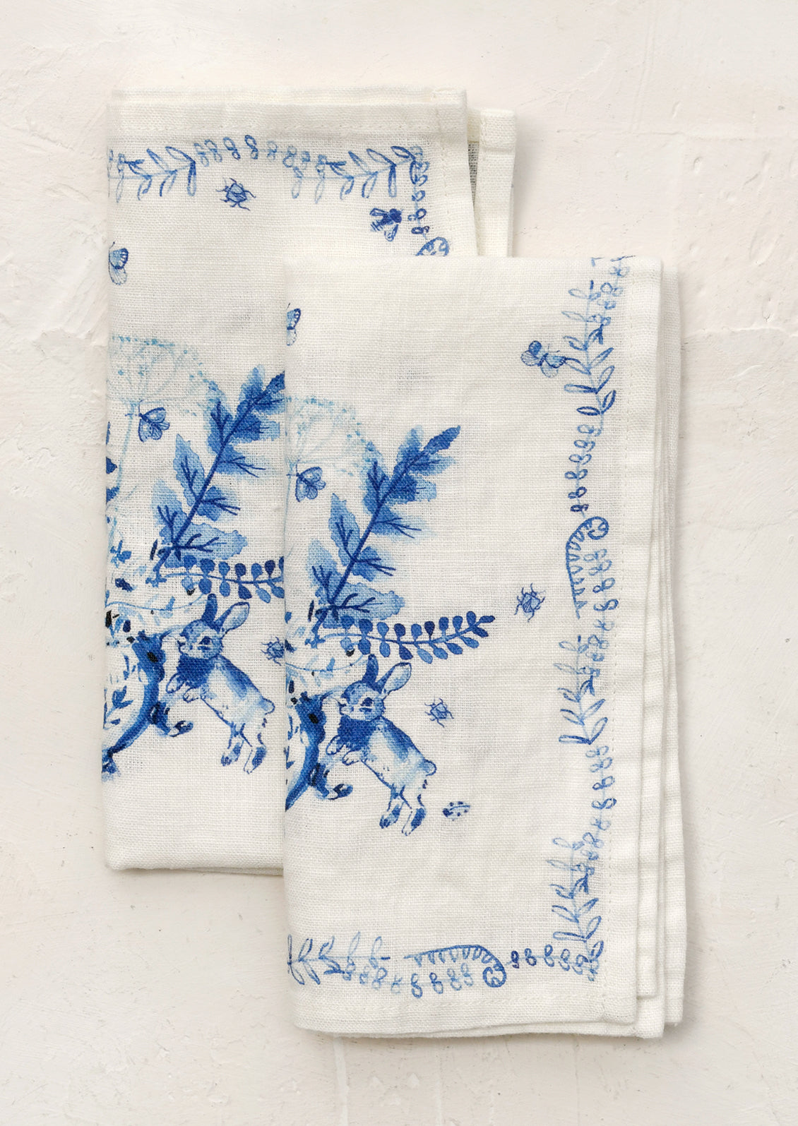 White napkins with blue floral and rabbit designs on a wooden surface