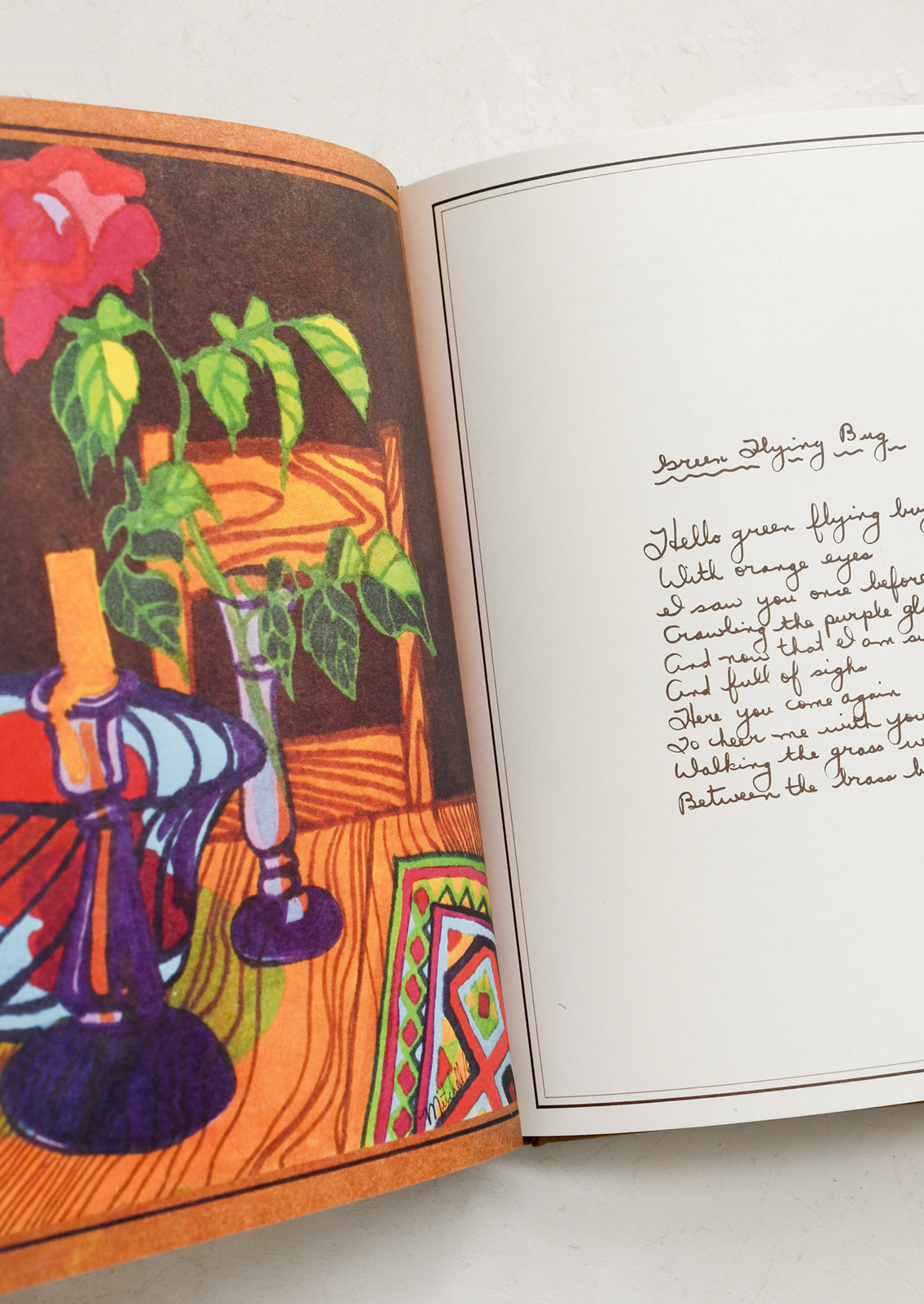 Open book with colorful illustration of a room and handwritten text on a white surface