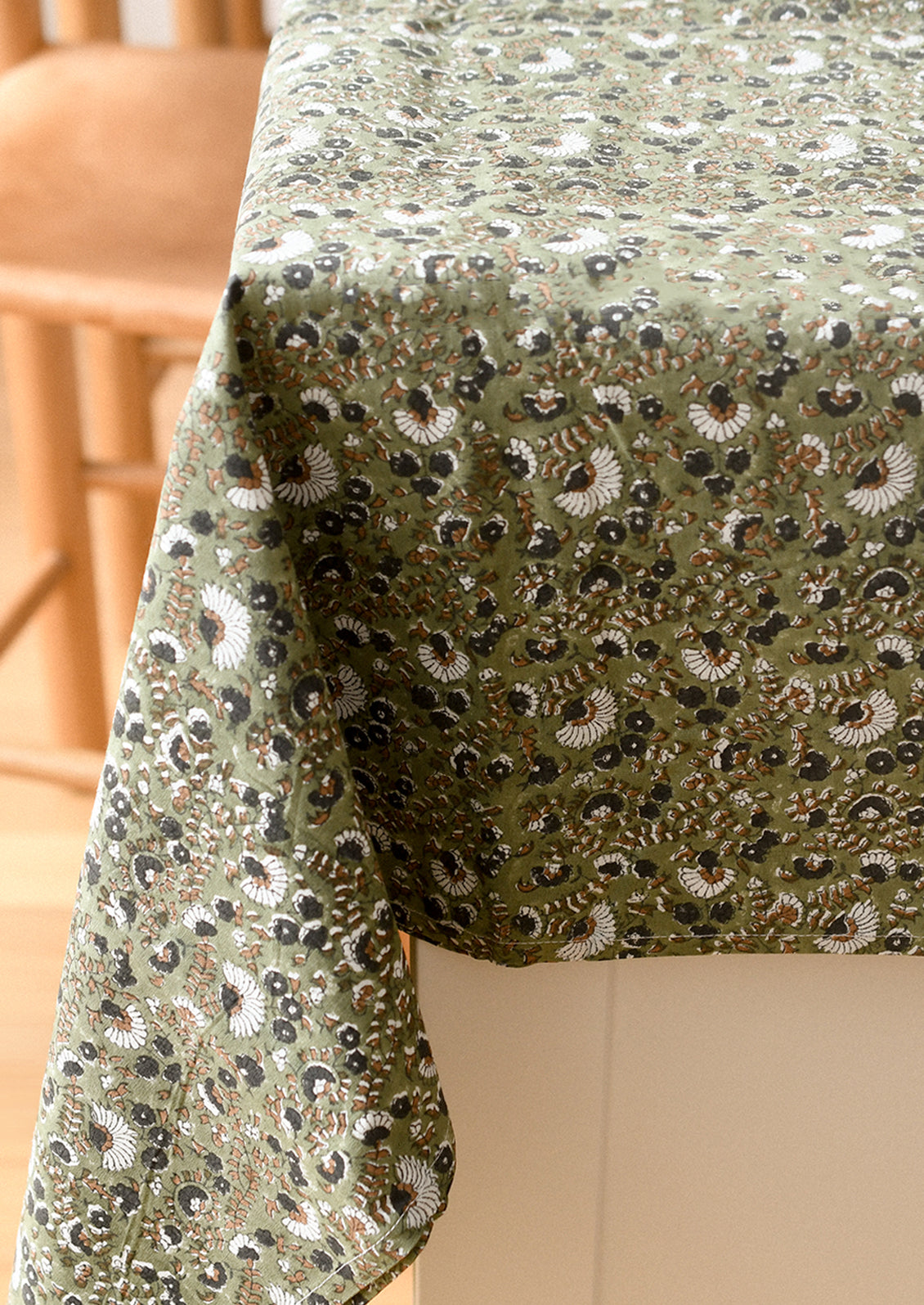 Close-up of a green tablecloth with floral patterns on a wooden chair.