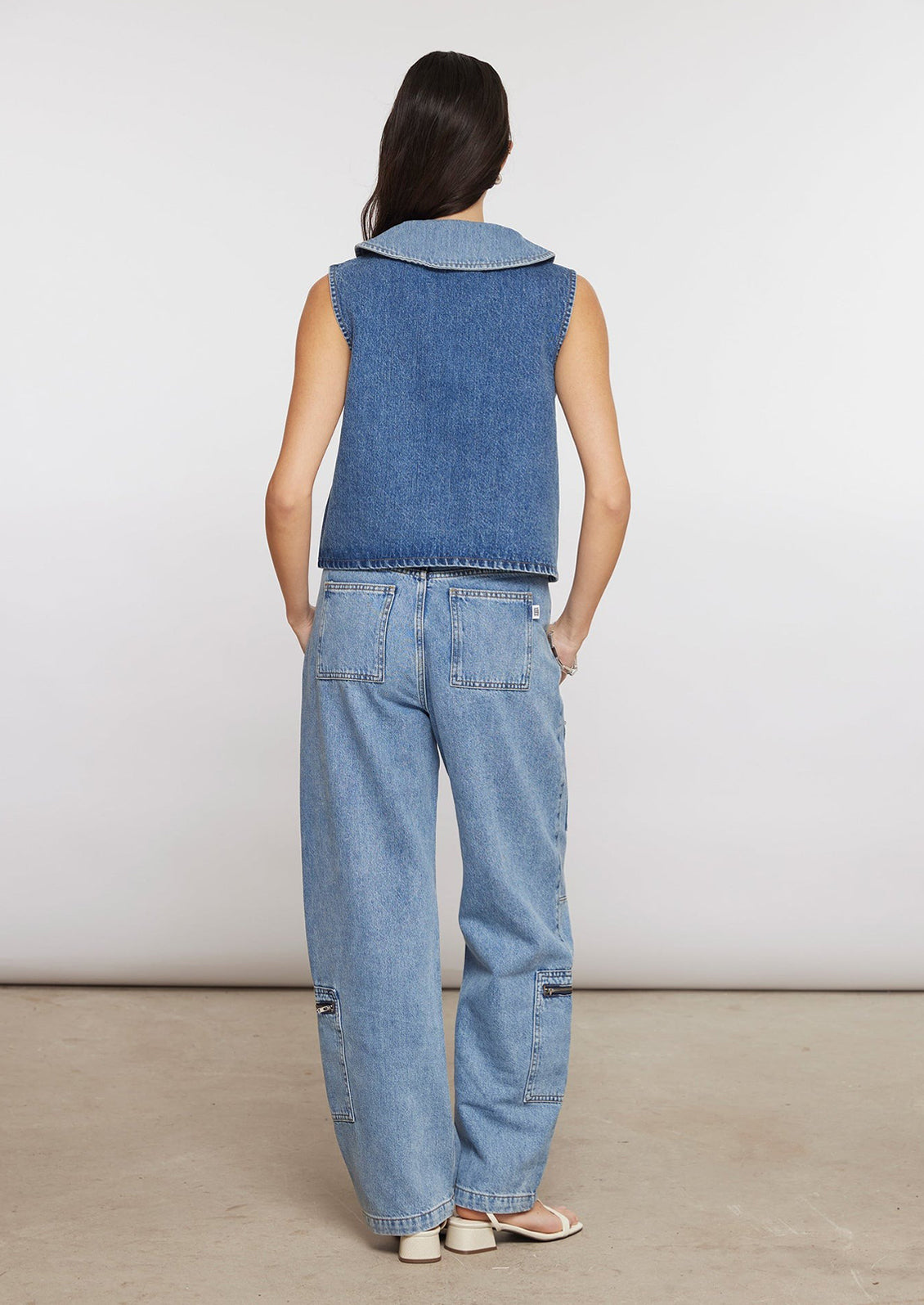 A person wearing light wash jeans with zip details on pockets.