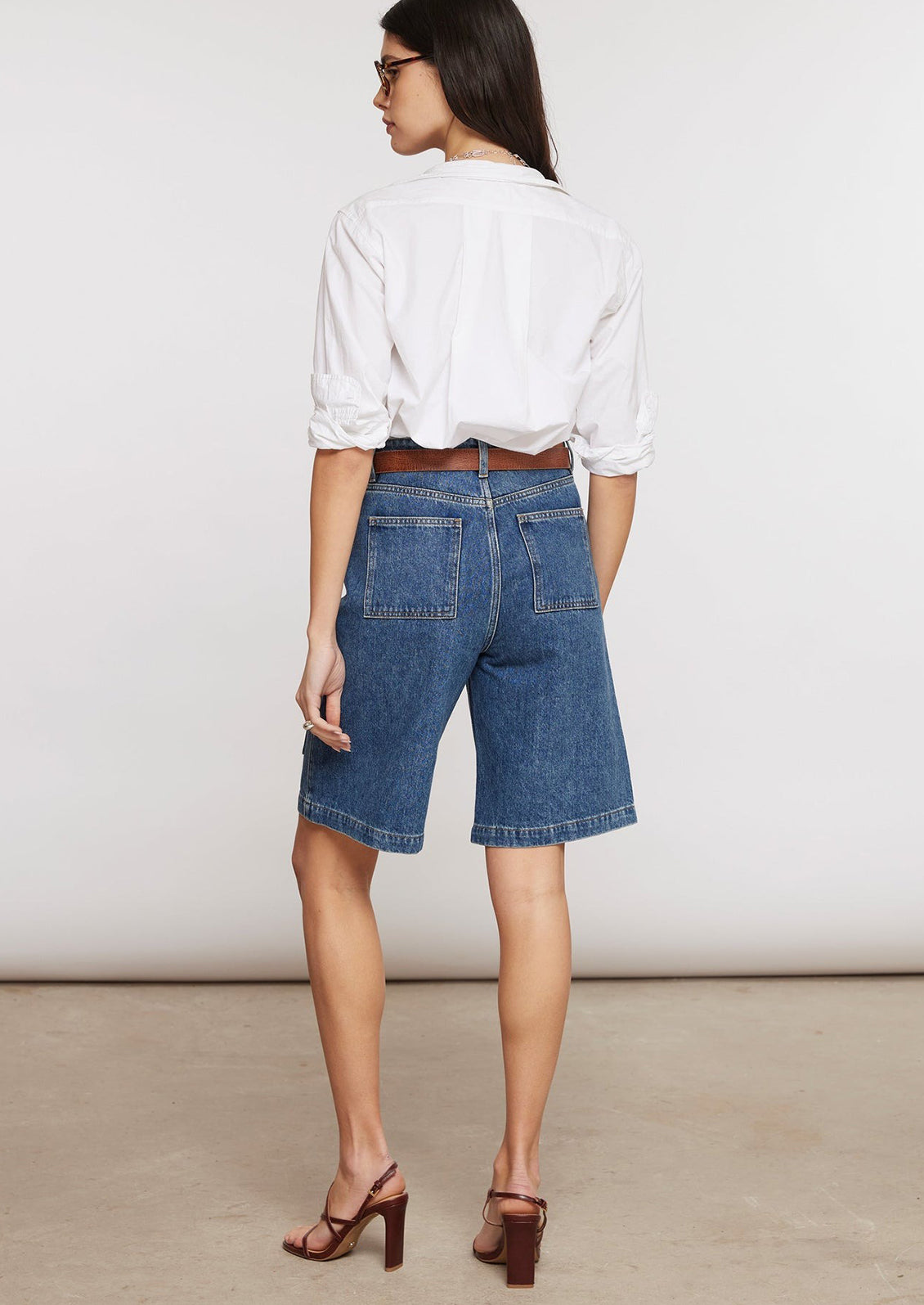 A person wearing a pair of knee-length denim shorts with zip details on patch pockets.