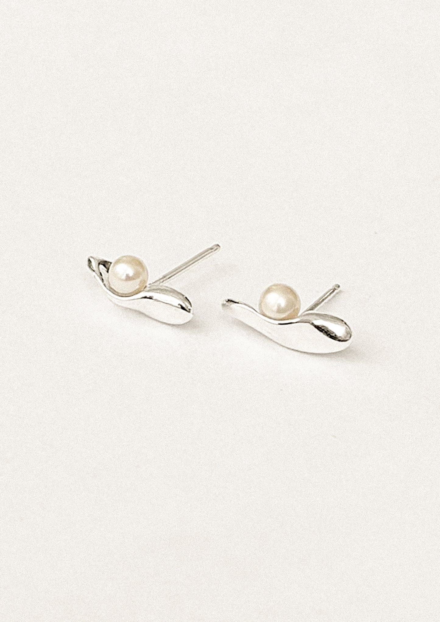 A pair of silver sliver shaped stud earrings with resting pearl.