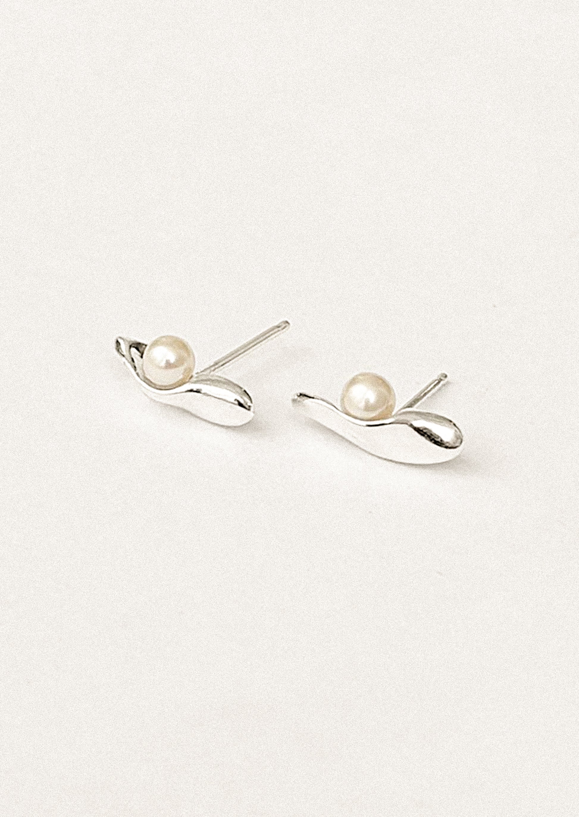 A pair of silver sliver shaped stud earrings with resting pearl.