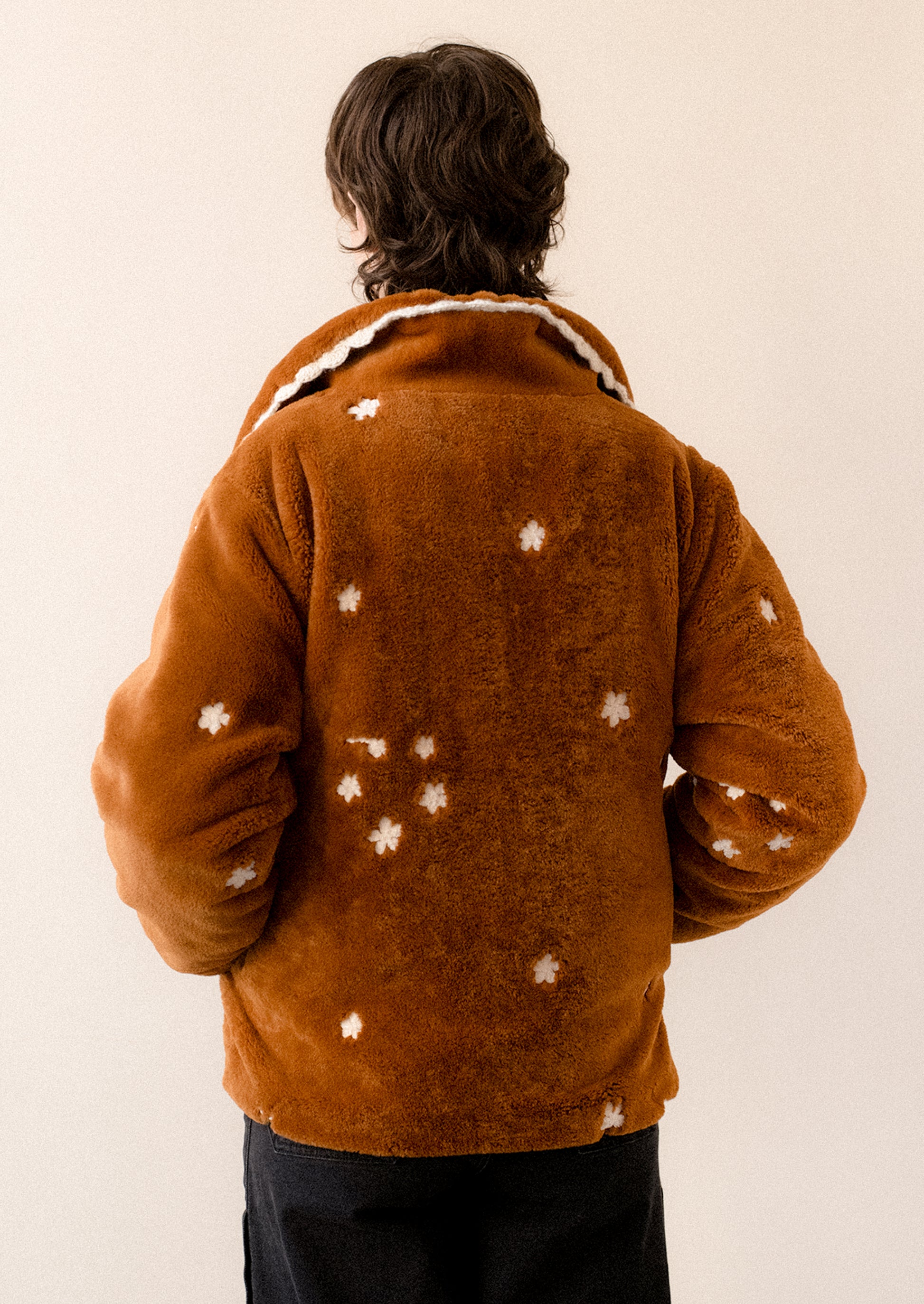 A woman wearing a caramel colored faux fur jacket with white floral embroidery and black toggle button front.