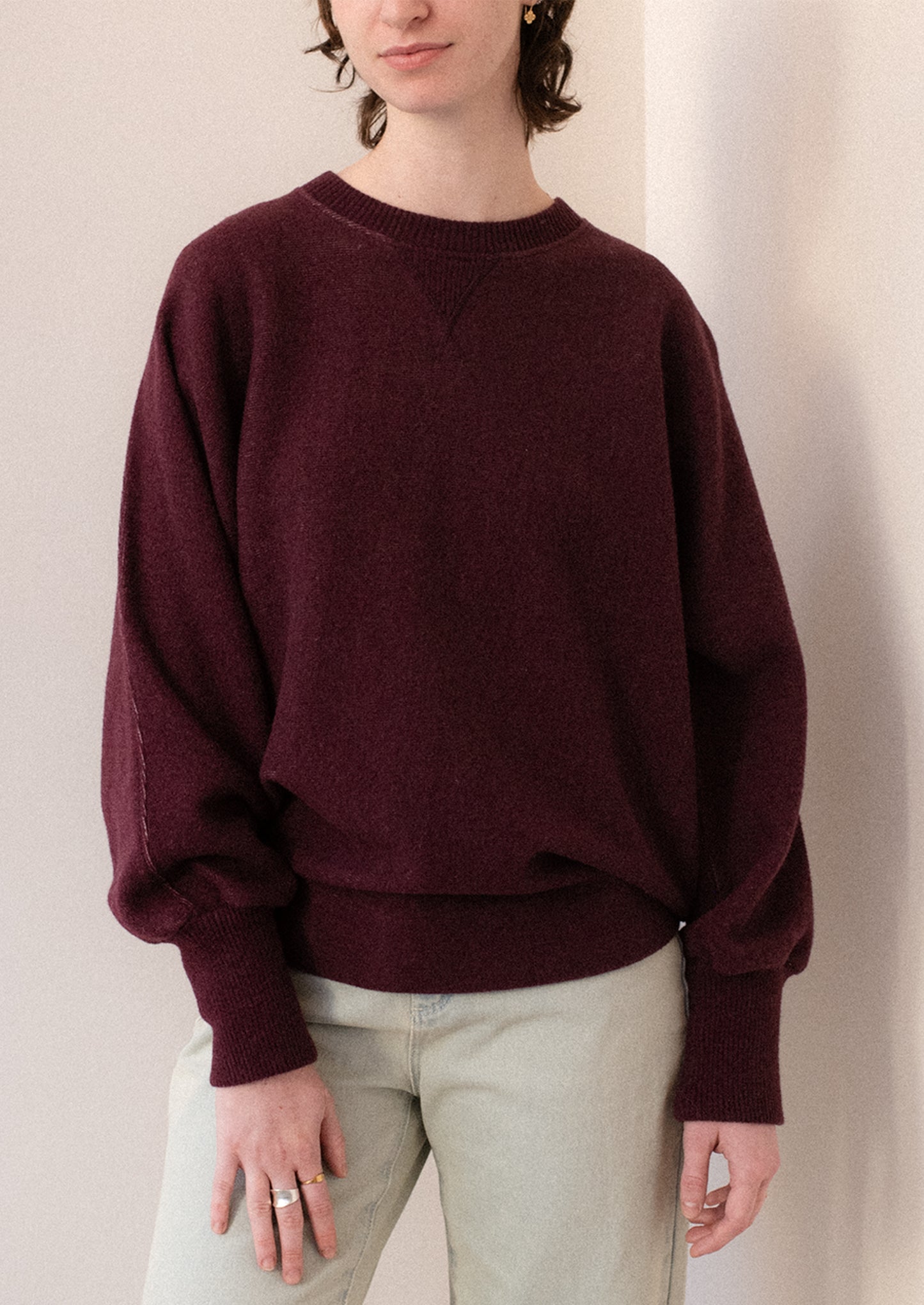 A woman wearing a sweater in burgundy with sweatshirt style silhouette.