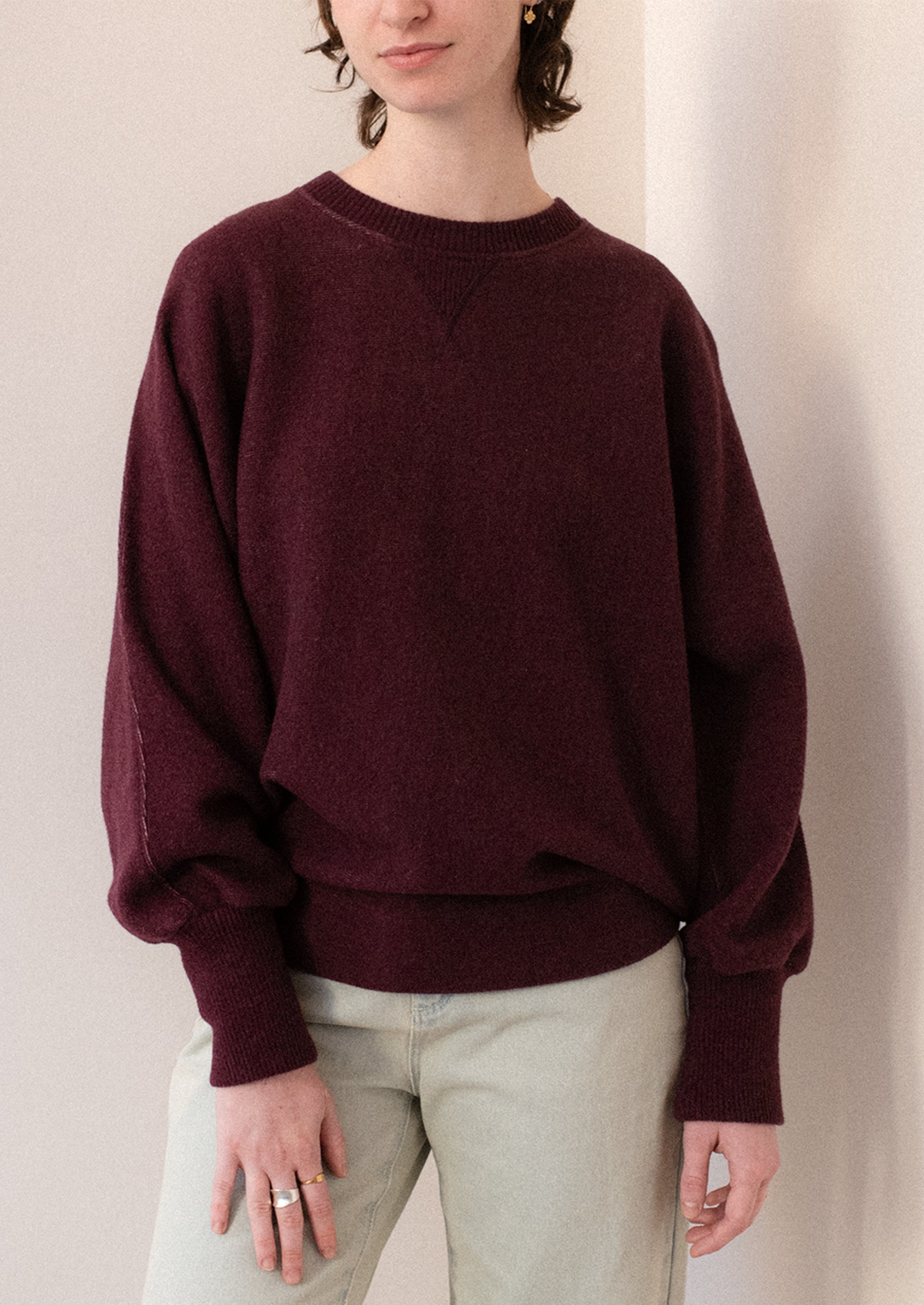 A woman wearing a sweater in burgundy with sweatshirt style silhouette.