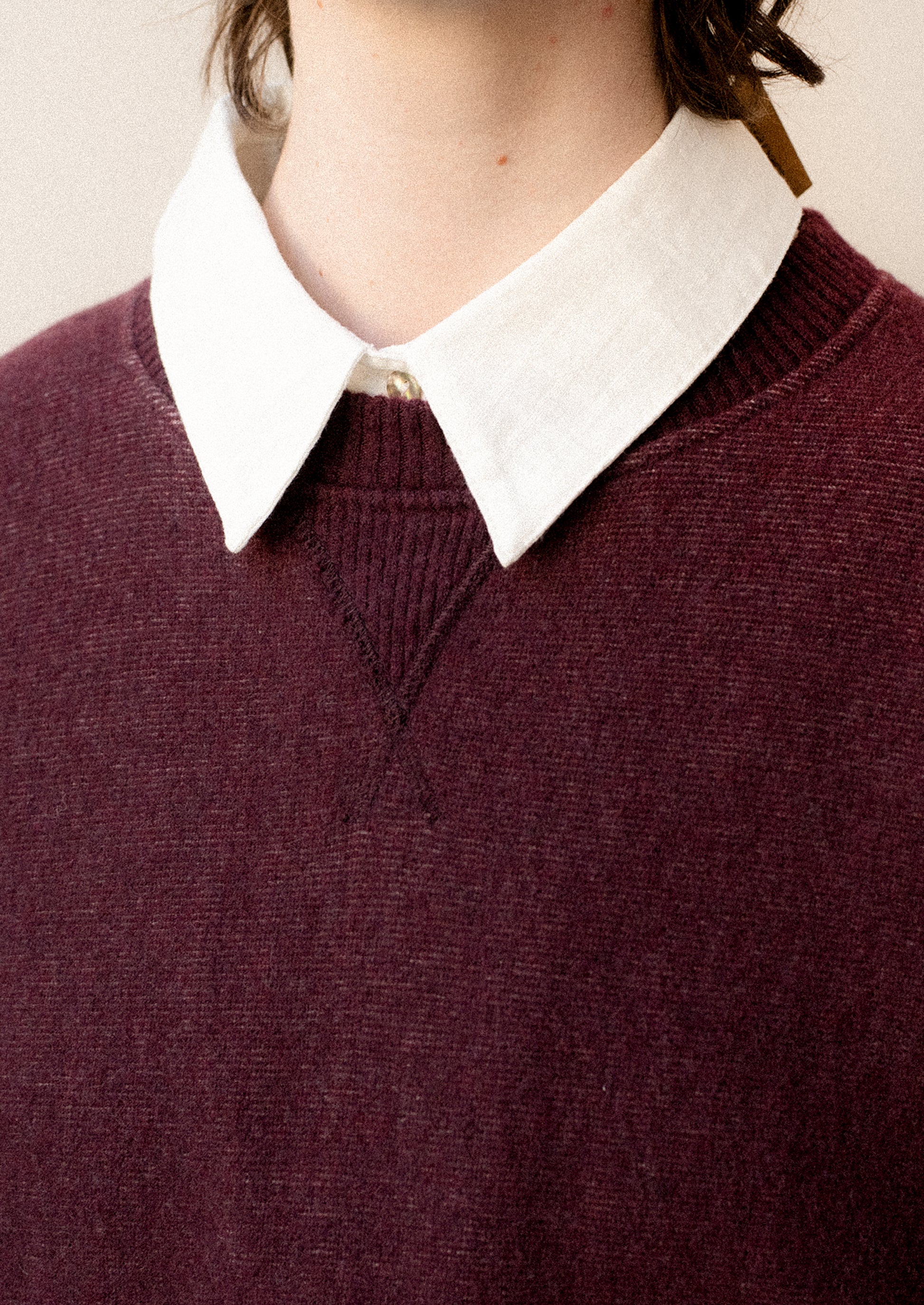 A woman wearing a sweater in burgundy with sweatshirt style silhouette.