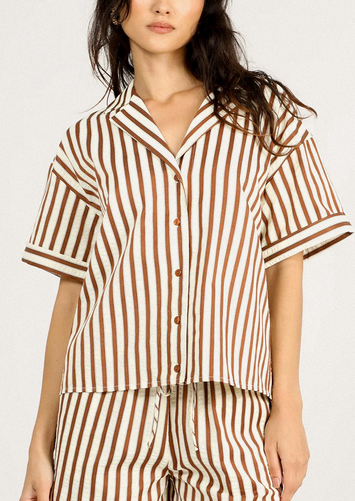 A person wearing a short sleeve button front shirt in cream and brown stripe.