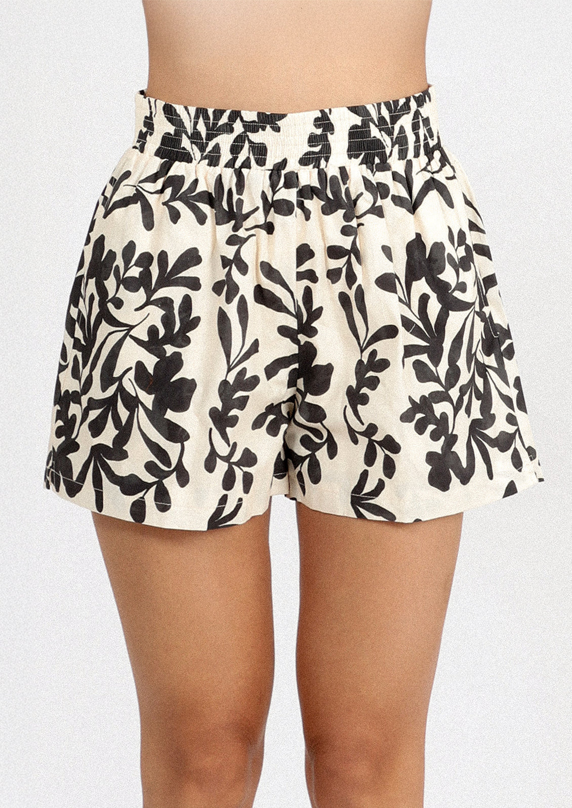 A person wearing a white pair of shorts with black leafy floral print.
