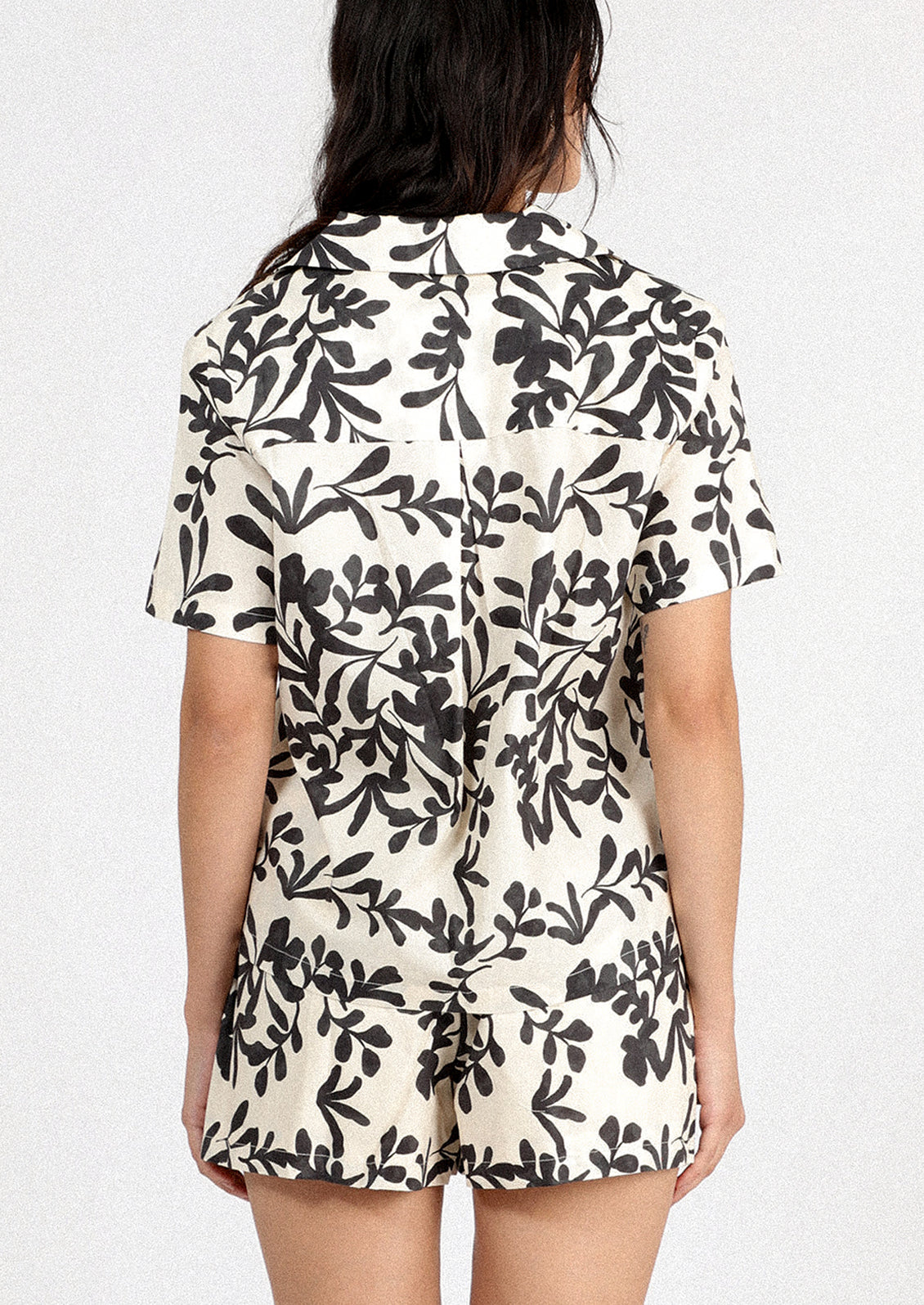 A person wearing a white short sleeve shirt with black leafy floral print.