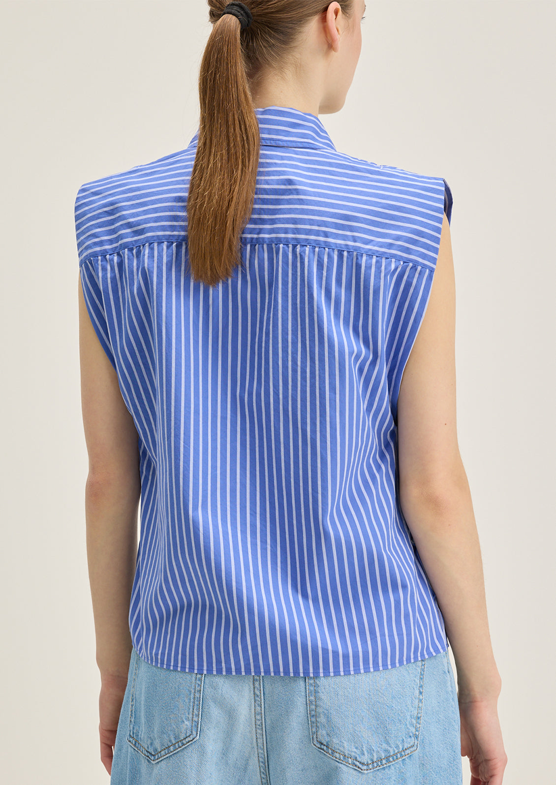 A woman wearing a sleeveless blue striped button down collared shirt.