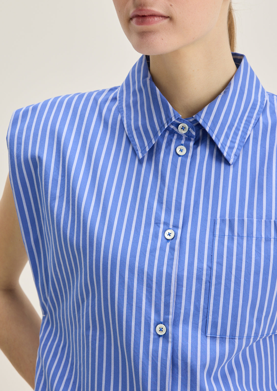 A woman wearing a sleeveless blue striped button down collared shirt.