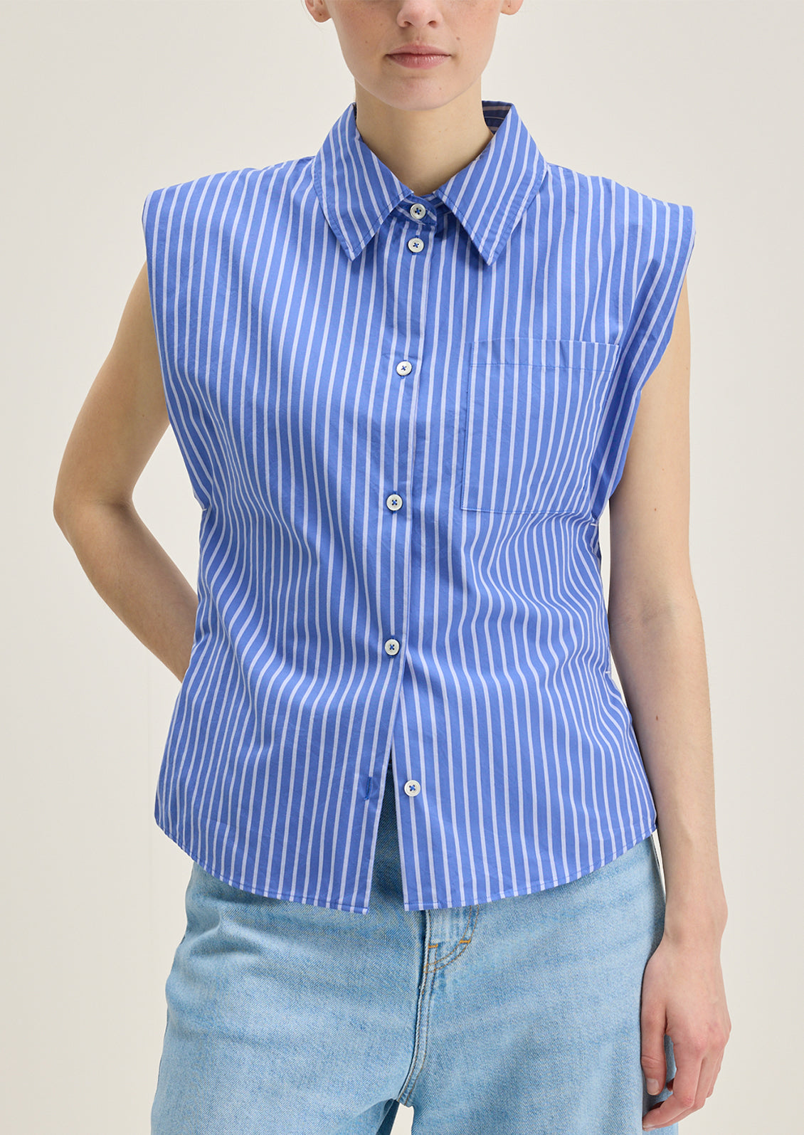 A woman wearing a sleeveless blue striped button down collared shirt.