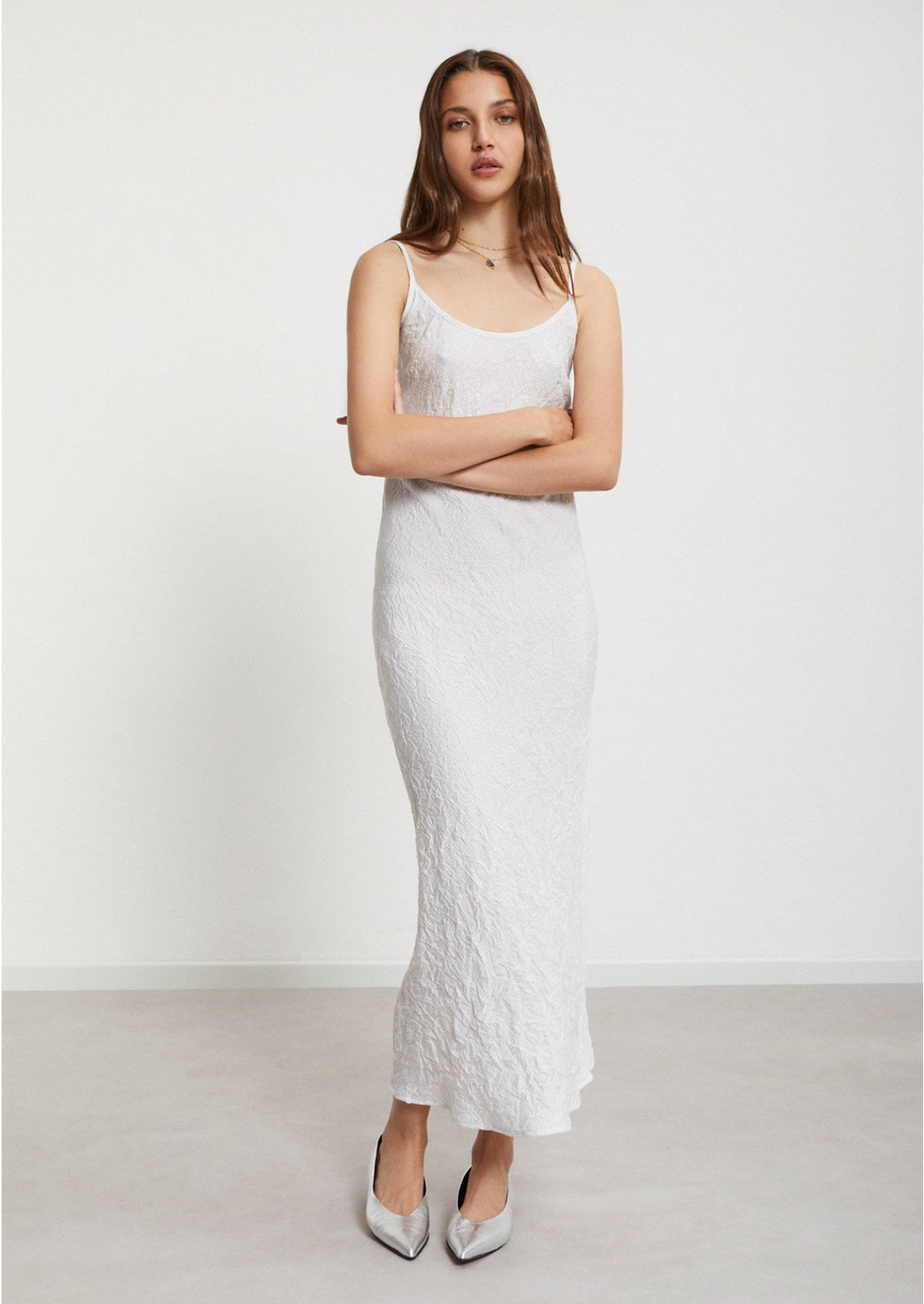 A woman wearing a white dress with crinkled texture and diagonal pinstripe pattern.