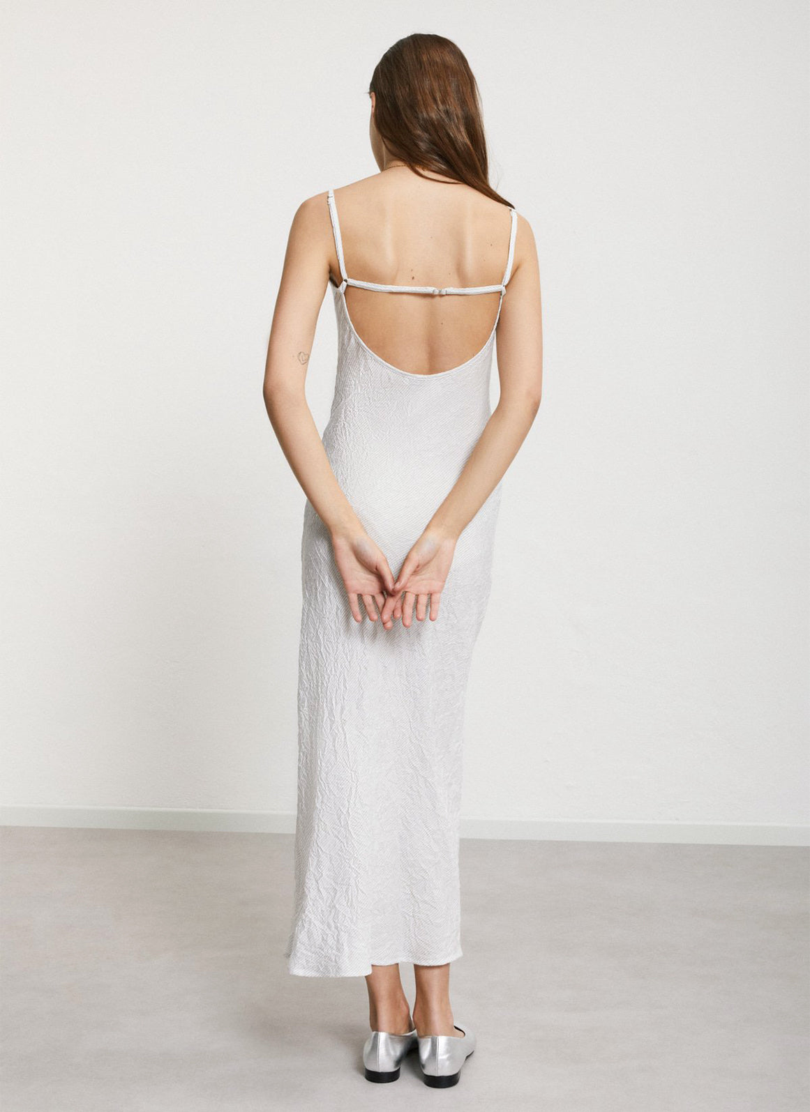 A woman wearing a white dress with crinkled texture and diagonal pinstripe pattern.