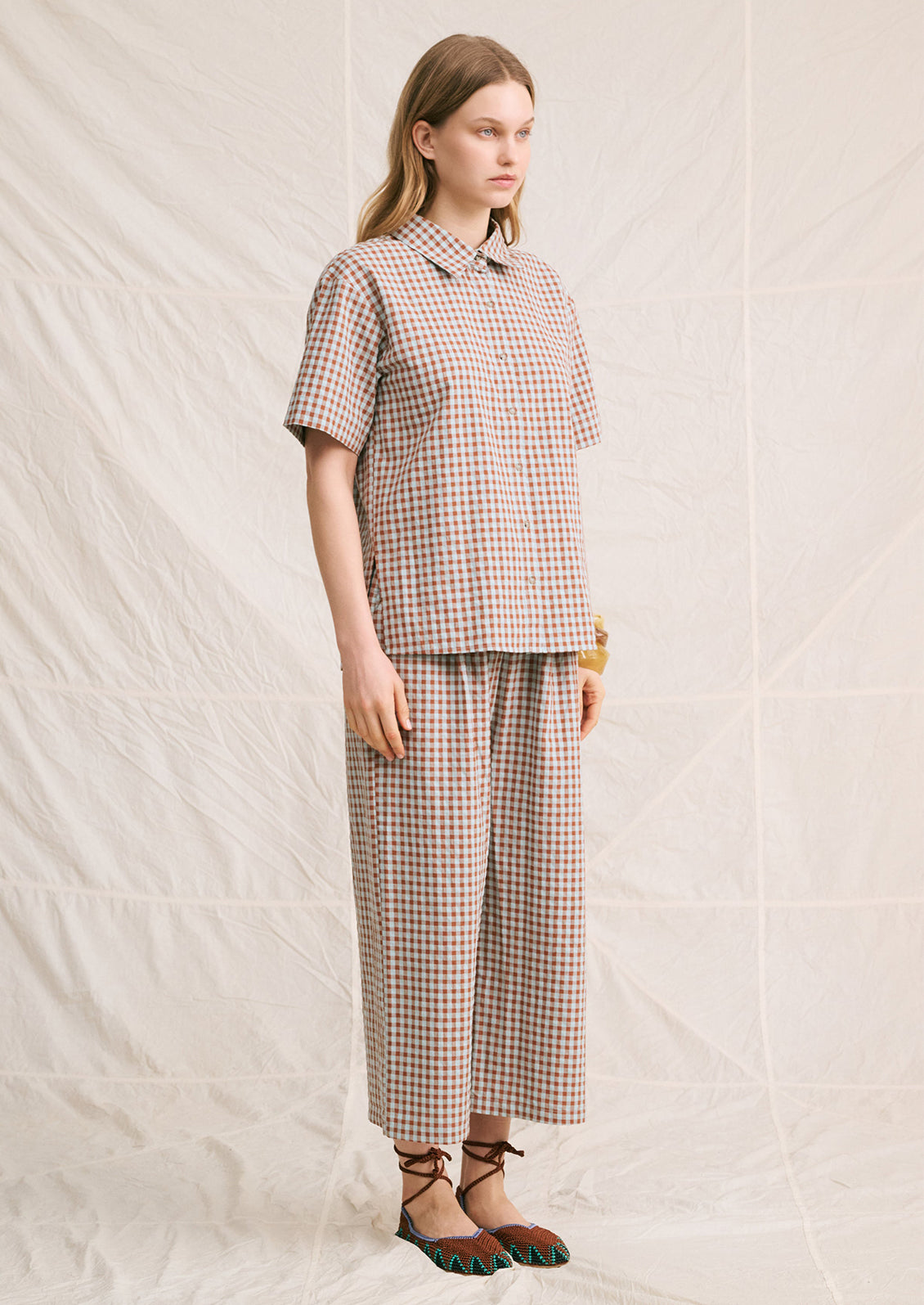 A woman wearing a short sleeve collared shirt in aqua and brown gingham pattern.