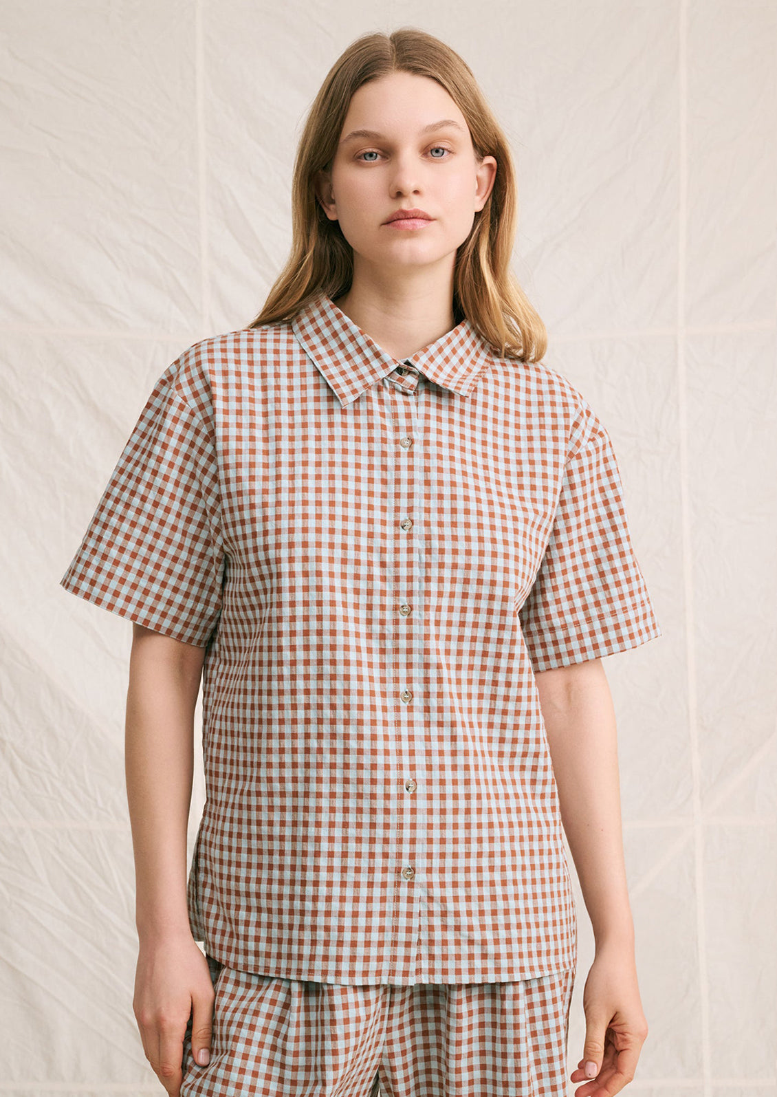 A woman wearing a short sleeve collared shirt in aqua and brown gingham pattern.