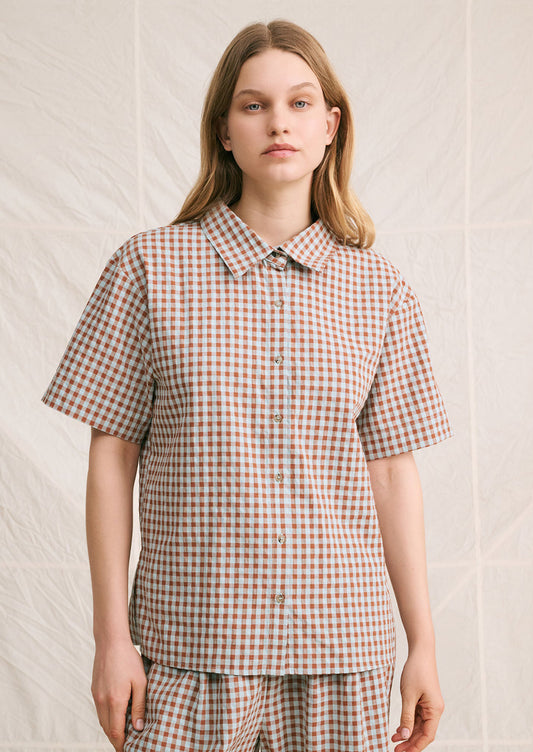 A woman wearing a short sleeve collared shirt in aqua and brown gingham pattern.
