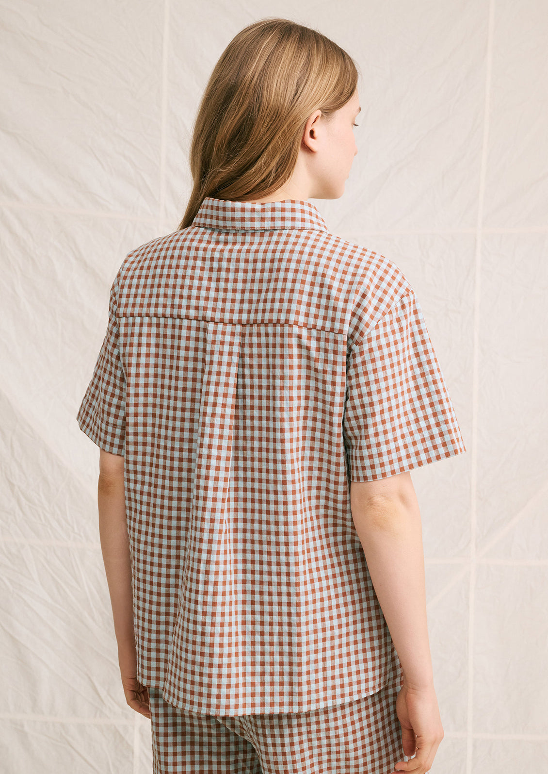 A woman wearing a short sleeve collared shirt in aqua and brown gingham pattern.