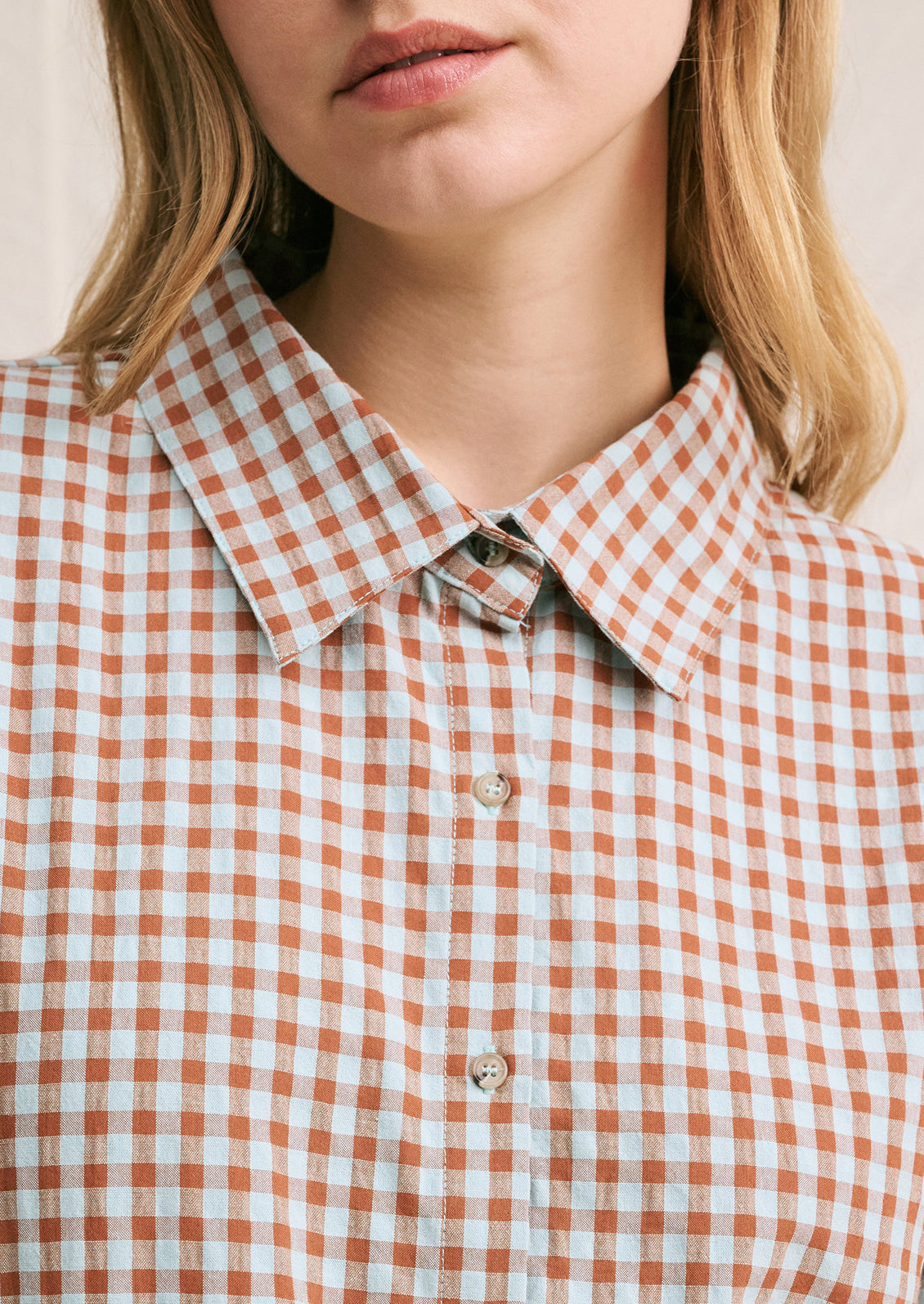 A woman wearing a short sleeve collared shirt in aqua and brown gingham pattern.