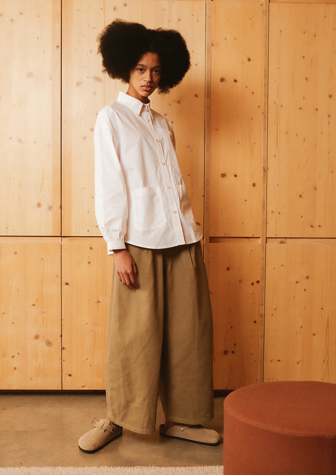 A woman wearing a pair of pleat front, balloon leg jeans in olive brown color.