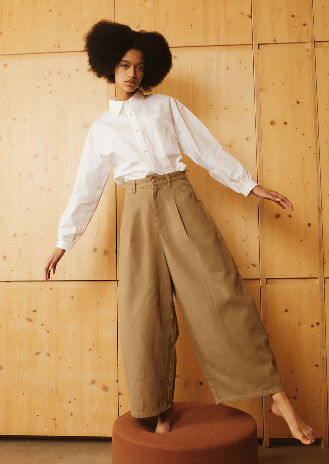 A woman wearing a pair of pleat front, balloon leg jeans in olive brown color.
