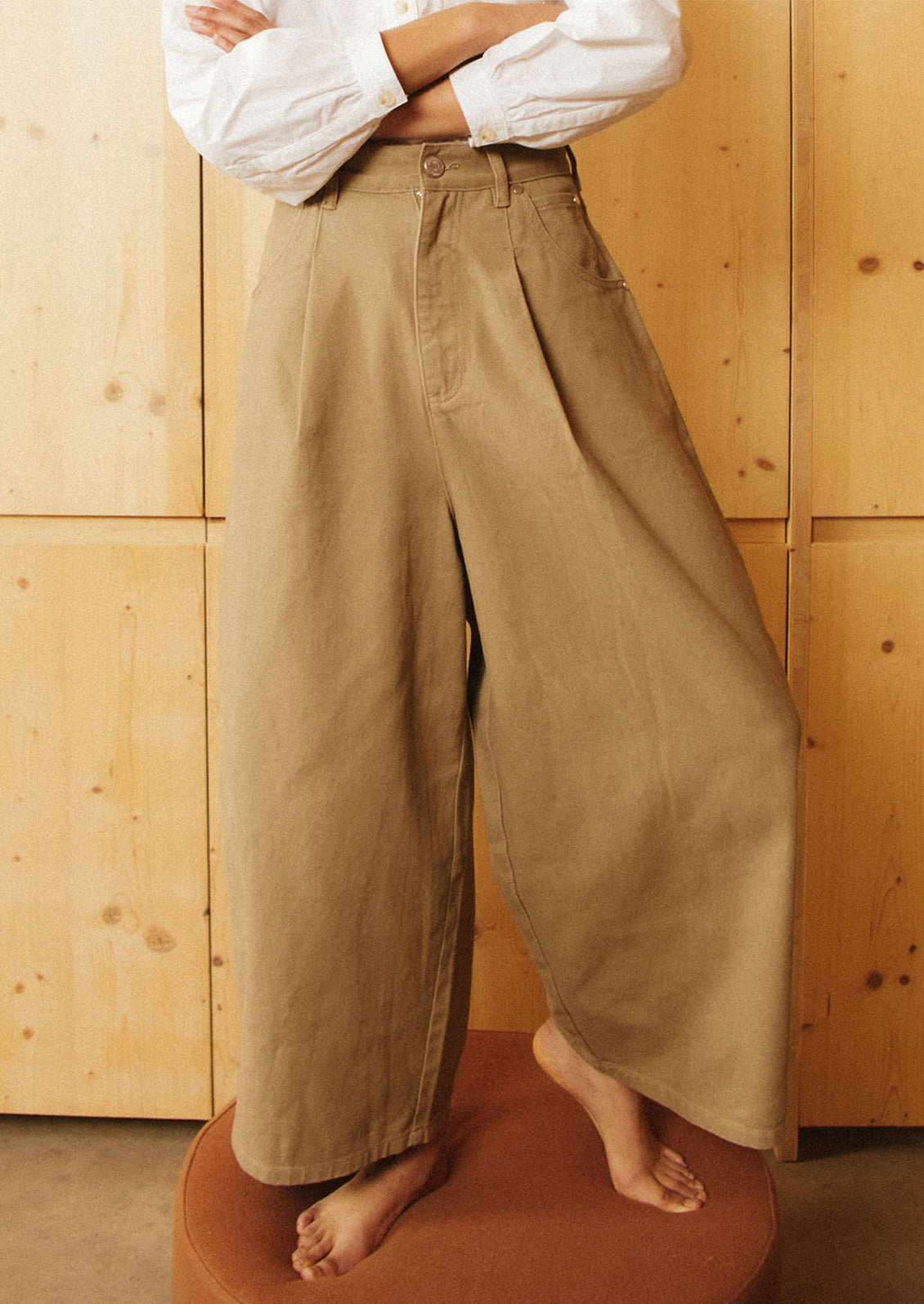 A woman wearing a pair of pleat front, balloon leg jeans in olive brown color.