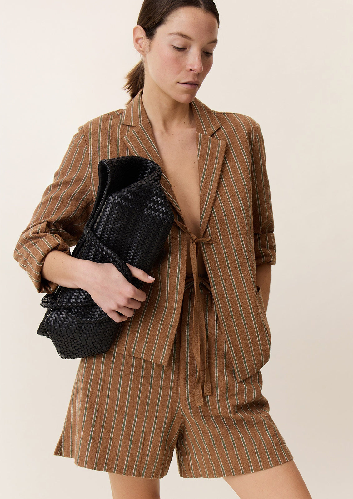 A woman wearing a brown suit jacket with green stripe pattern and tie front closure.