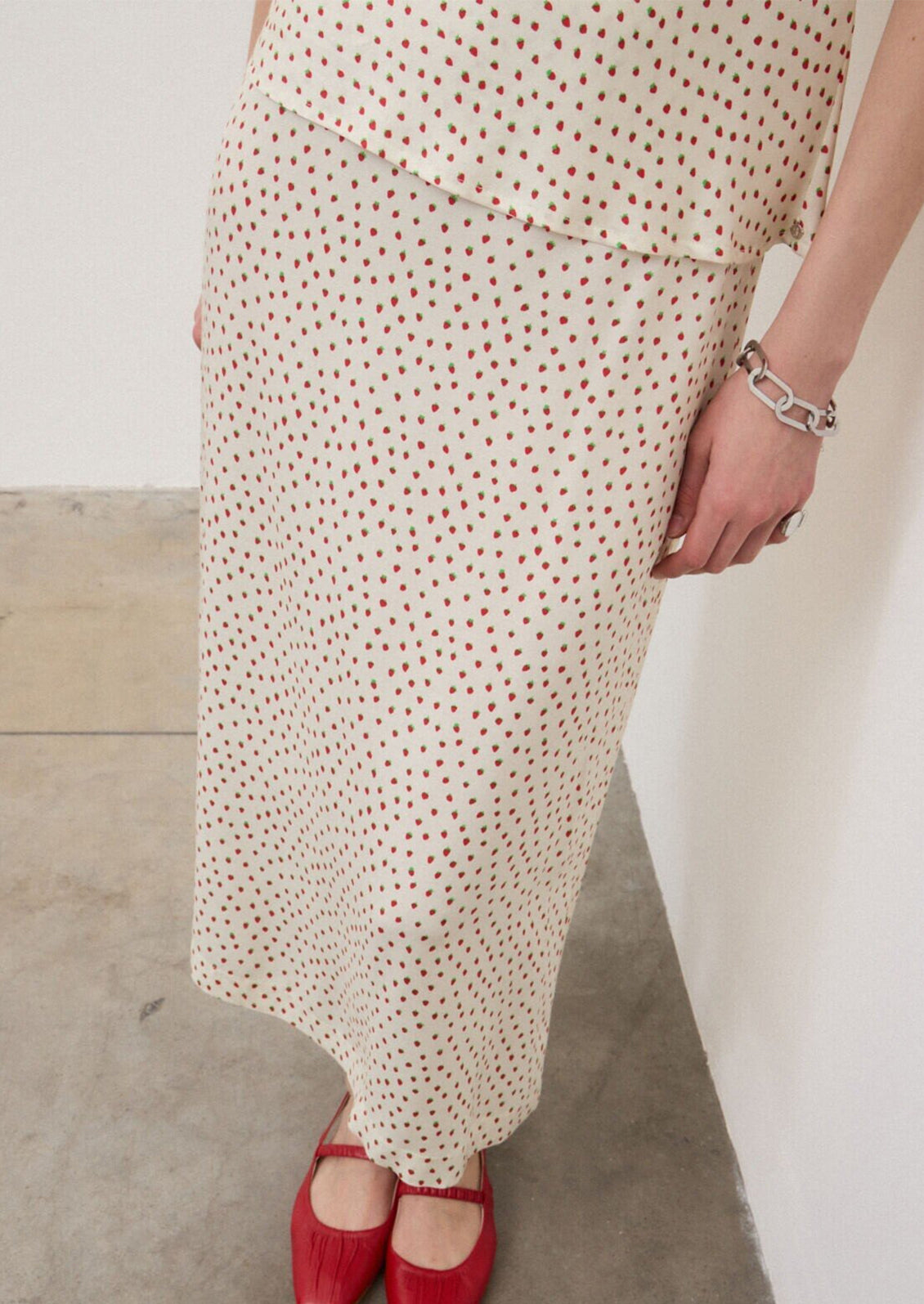 A person wearing an ivory slip skirt with small red strawberry print.