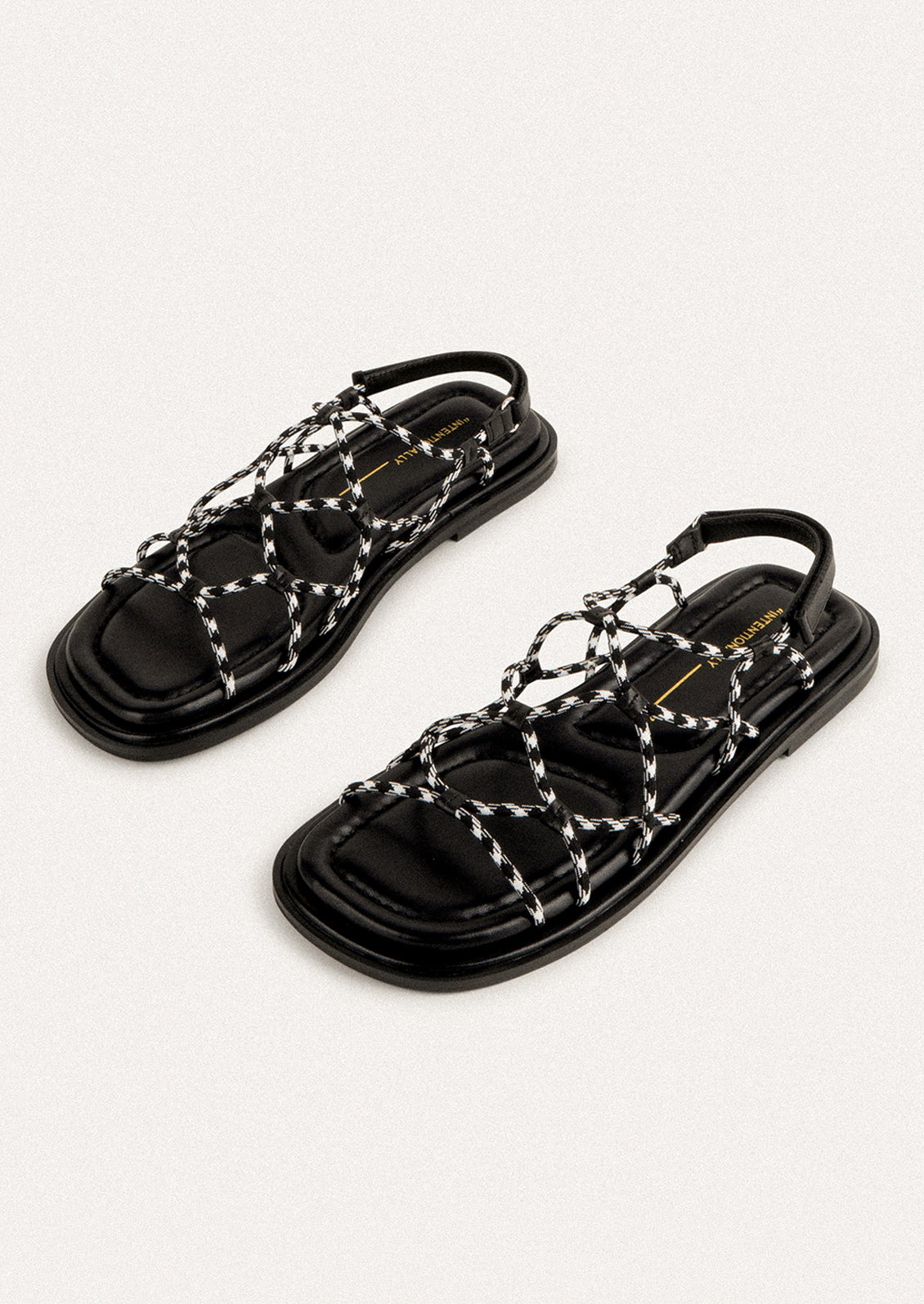 A pair of flat sandals with black and white paracord upper.