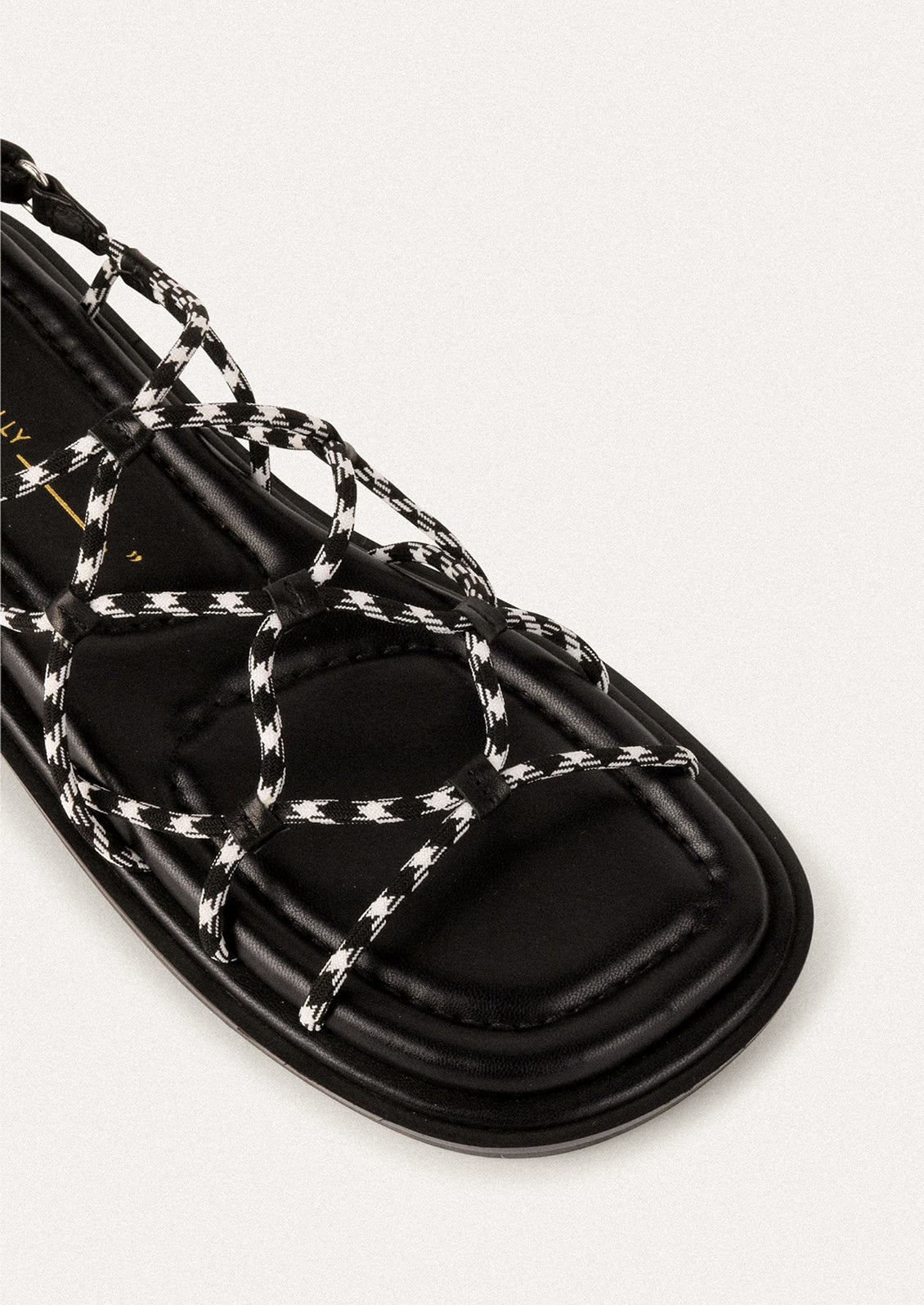 A pair of flat sandals with black and white paracord upper.