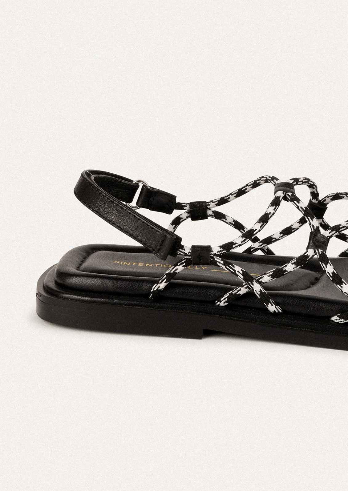 A pair of flat sandals with black and white paracord upper.