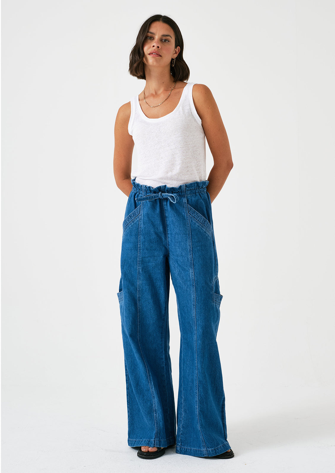 A woman wearing a pair of relaxed leg pants with cargo style details, in bright blue denim.