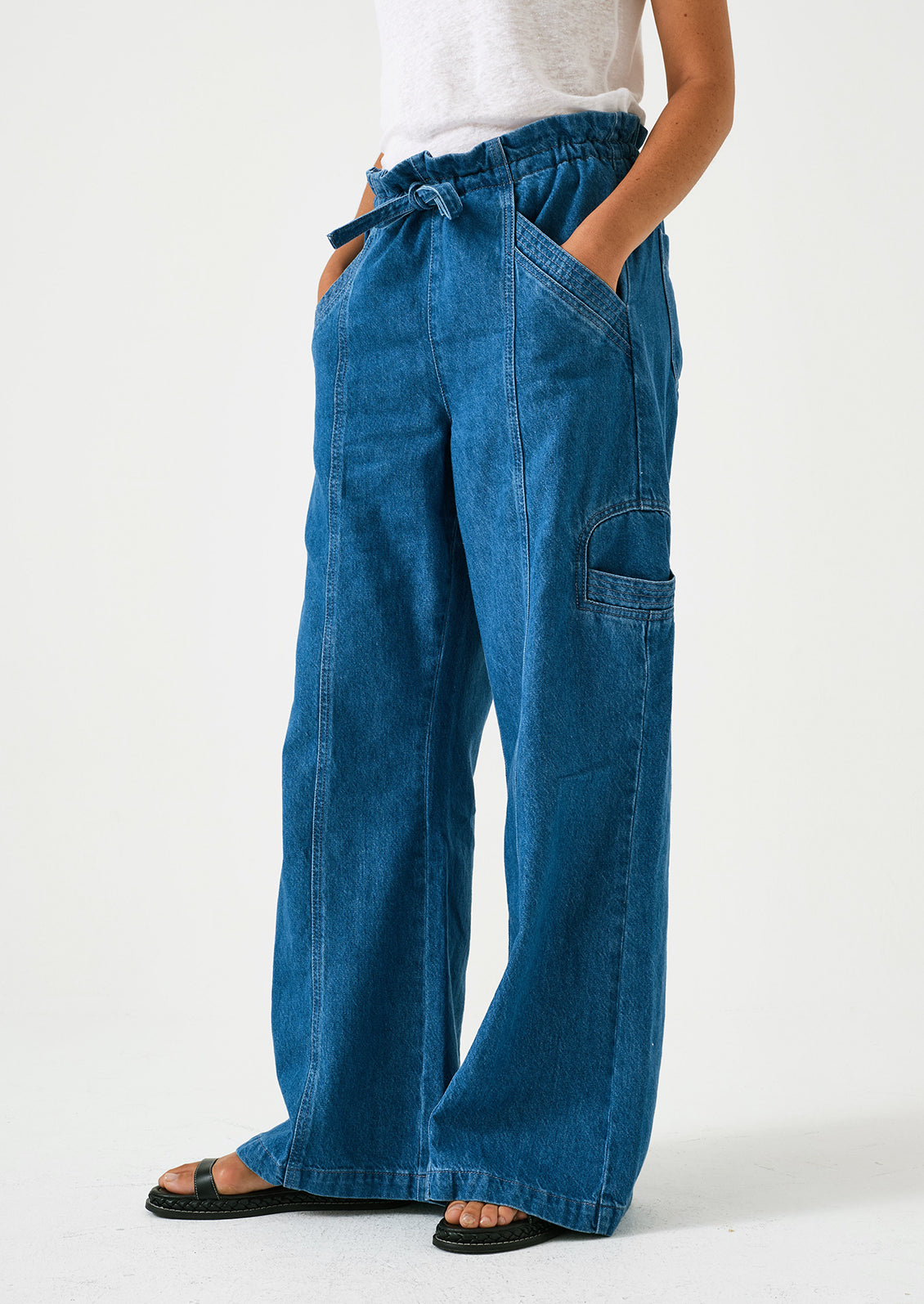 A woman wearing a pair of relaxed leg pants with cargo style details, in bright blue denim.