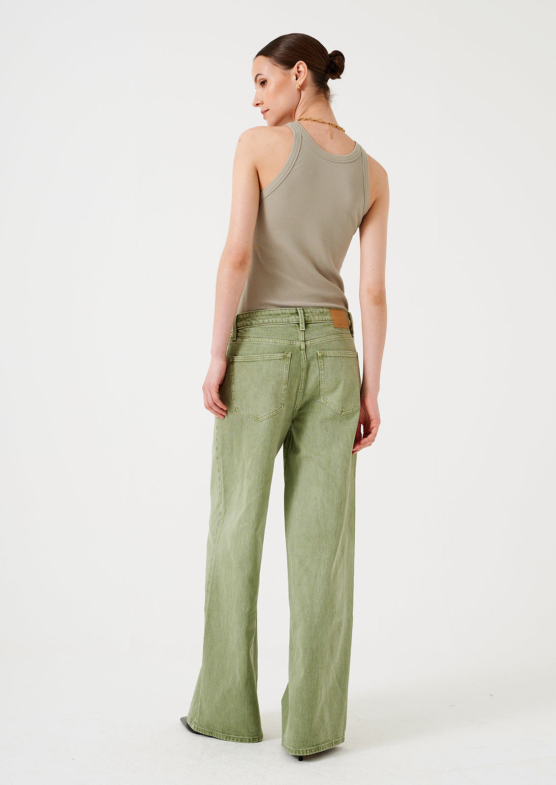 A woman wearing a pair of wide leg jeans in moss green wash.