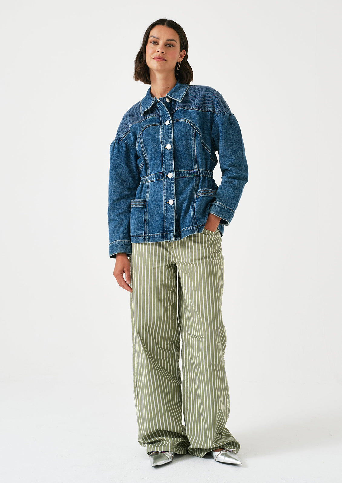 A woman wearing a denim jacket with decorative stitching and ruched shoulder detail.