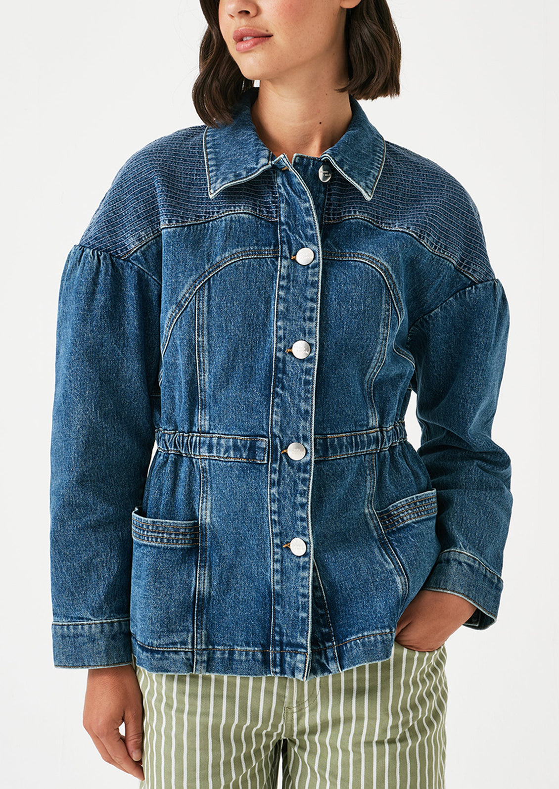 A woman wearing a denim jacket with decorative stitching and ruched shoulder detail.