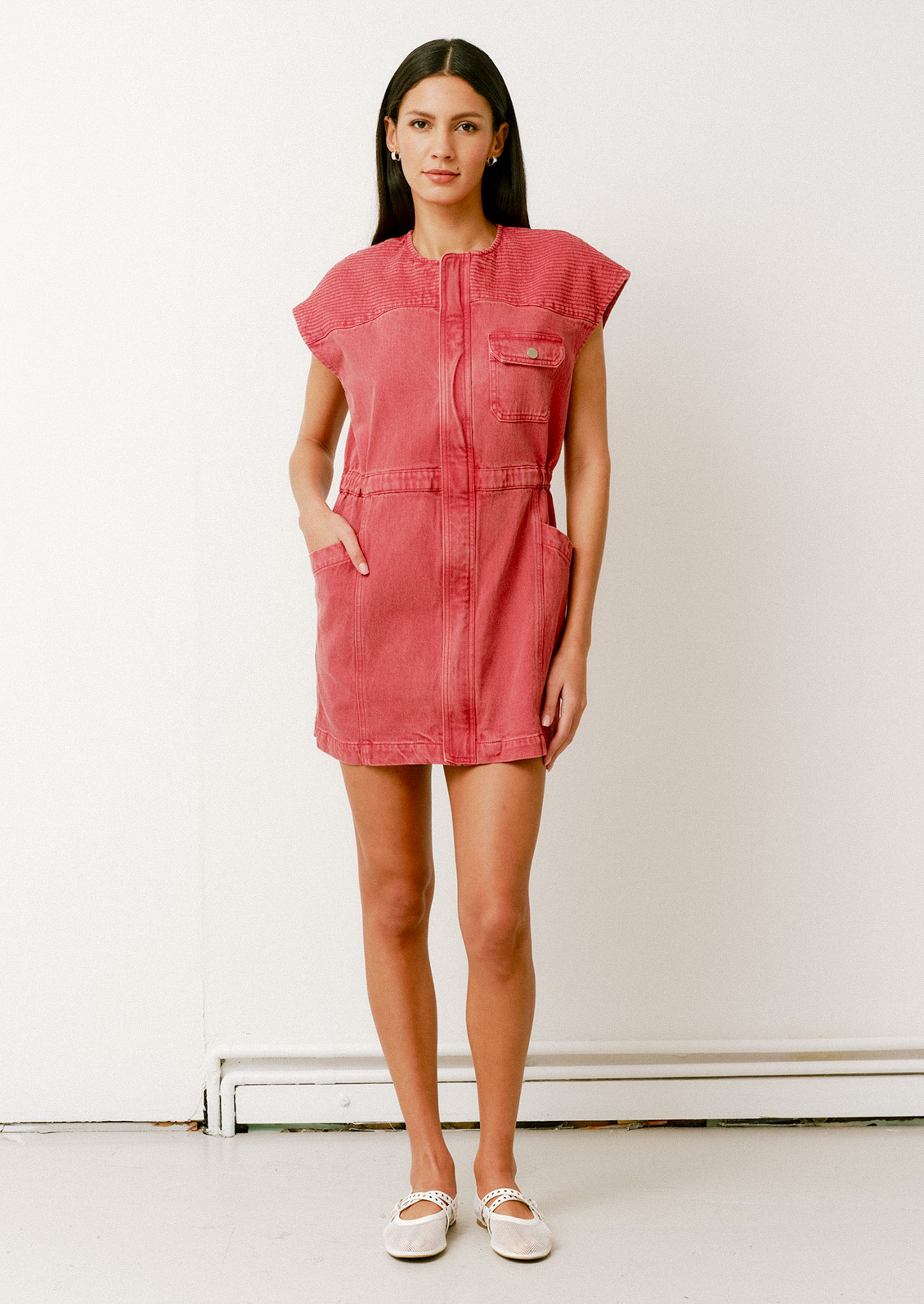 A person wearing a denim mini dress in red with cap sleeves and front pockets.